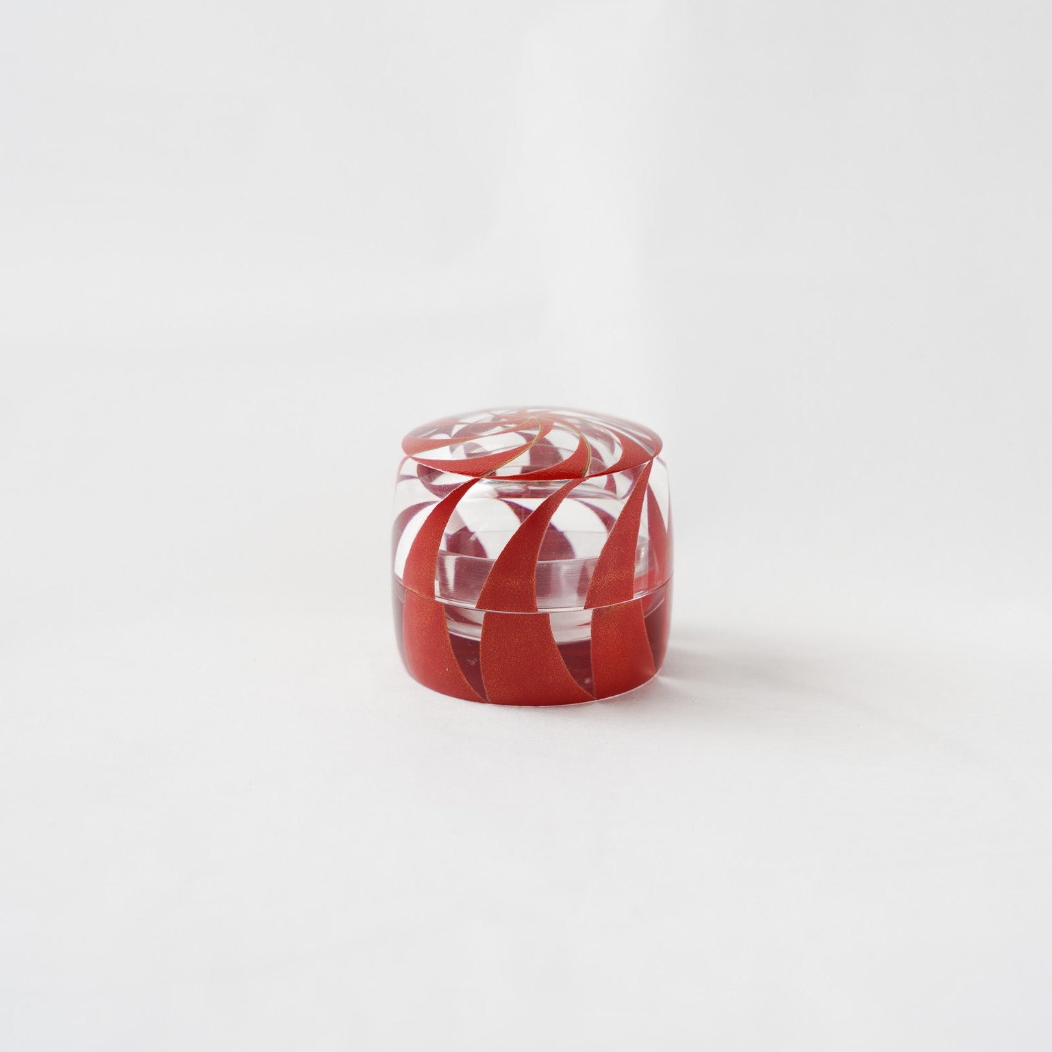 Front view of the #91 spiral acrylic small box by Hariya, showing the closed container with its vermilion and gold lacquer spiral patterns reflecting through the transparent resin body.