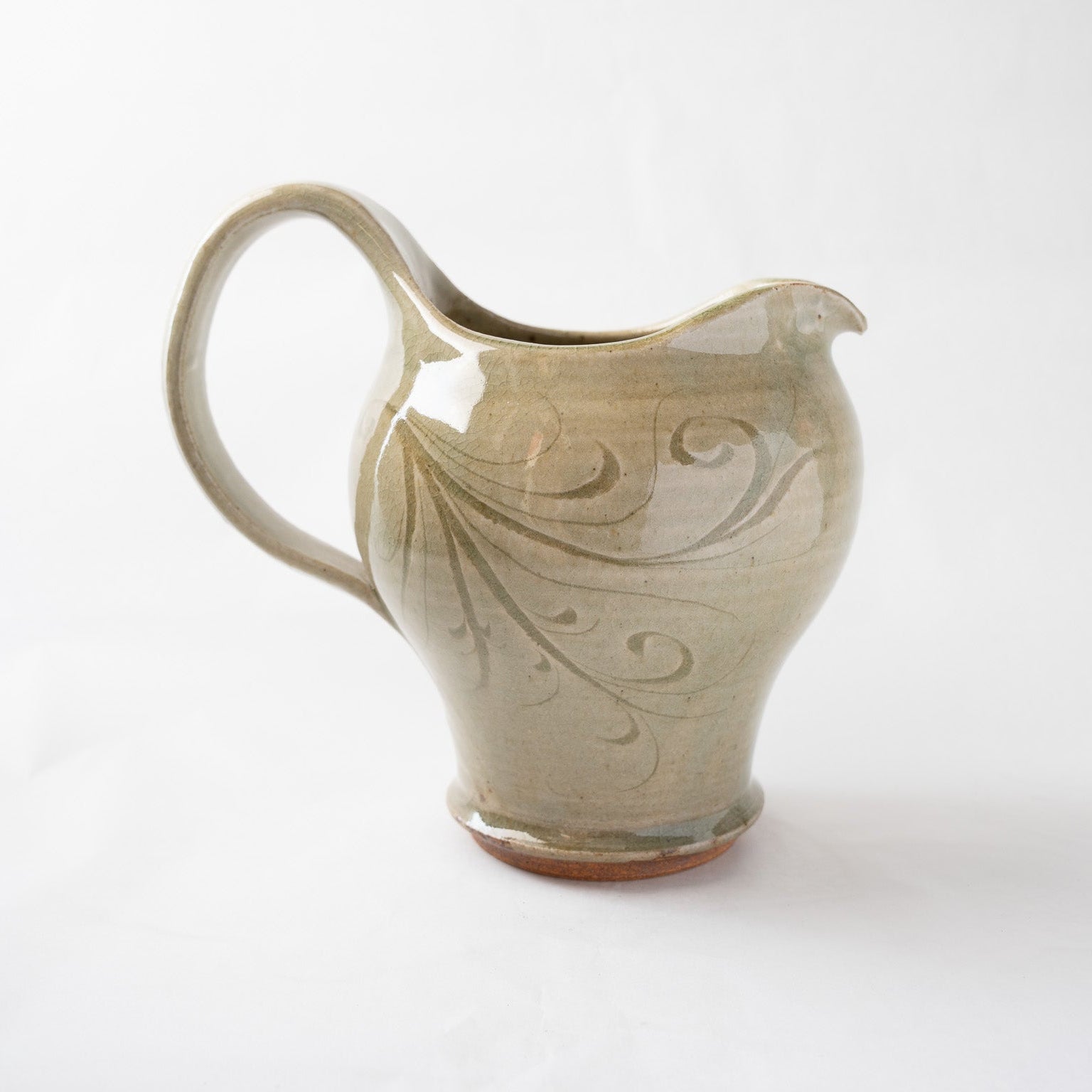 Opposite side profile of the incised ceramic pitcher, emphasizing the elegant junction where the handle meets the rim and the natural gradient of the ash-green glaze.