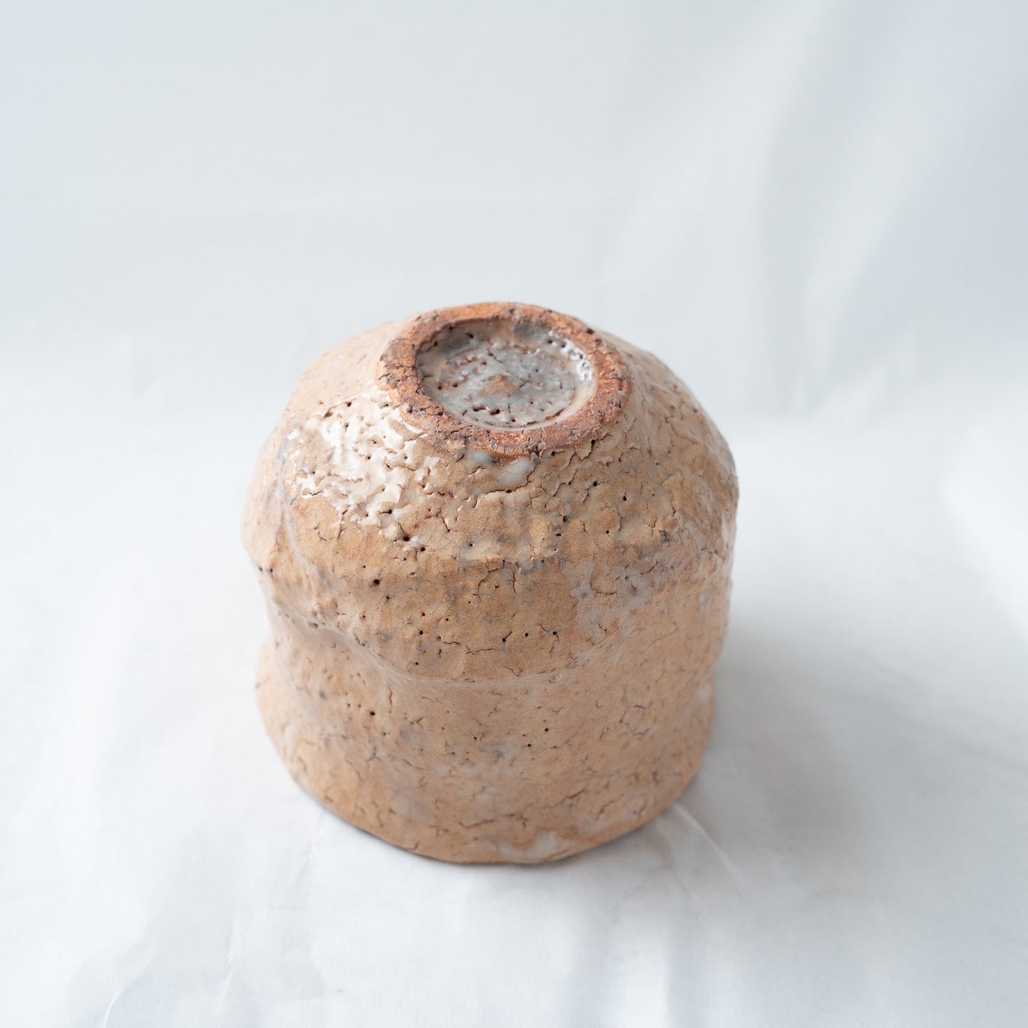 Close-up of the inverted base of the loquat-glazed cup, detailing the unglazed reddish clay foot ring and rustic, crawled white glaze textures.
