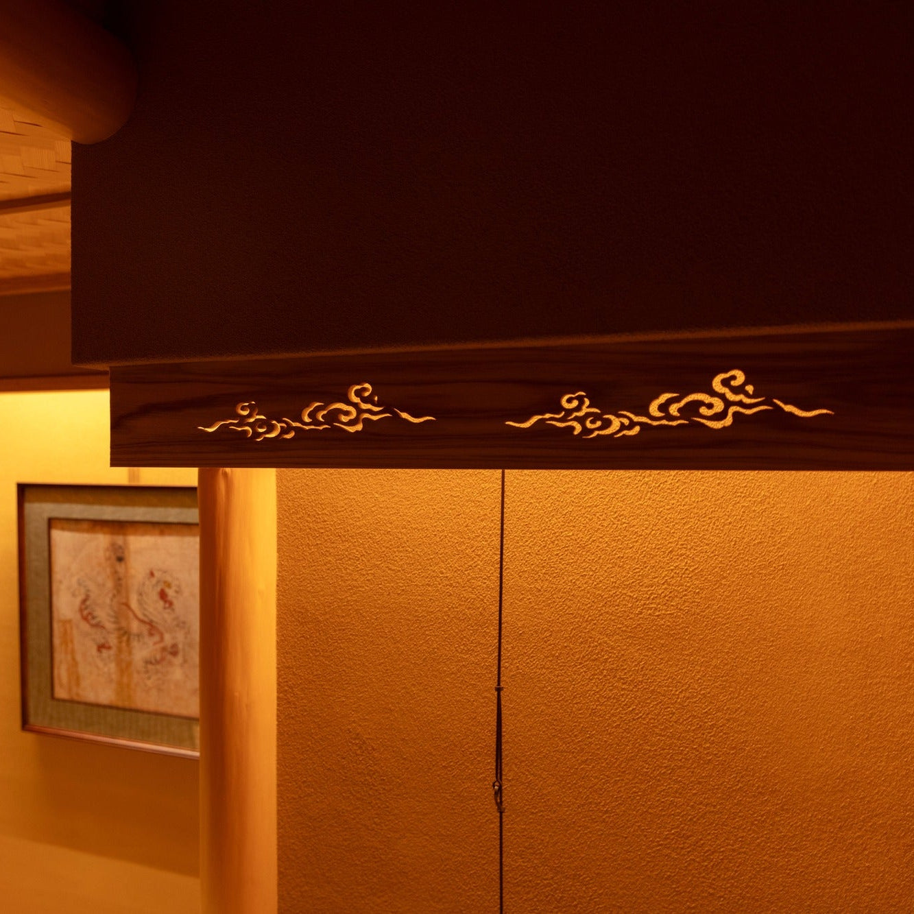 A timber transom carved with drifting clouds glows above a doorway, openwork joinery of Japanese architecture.