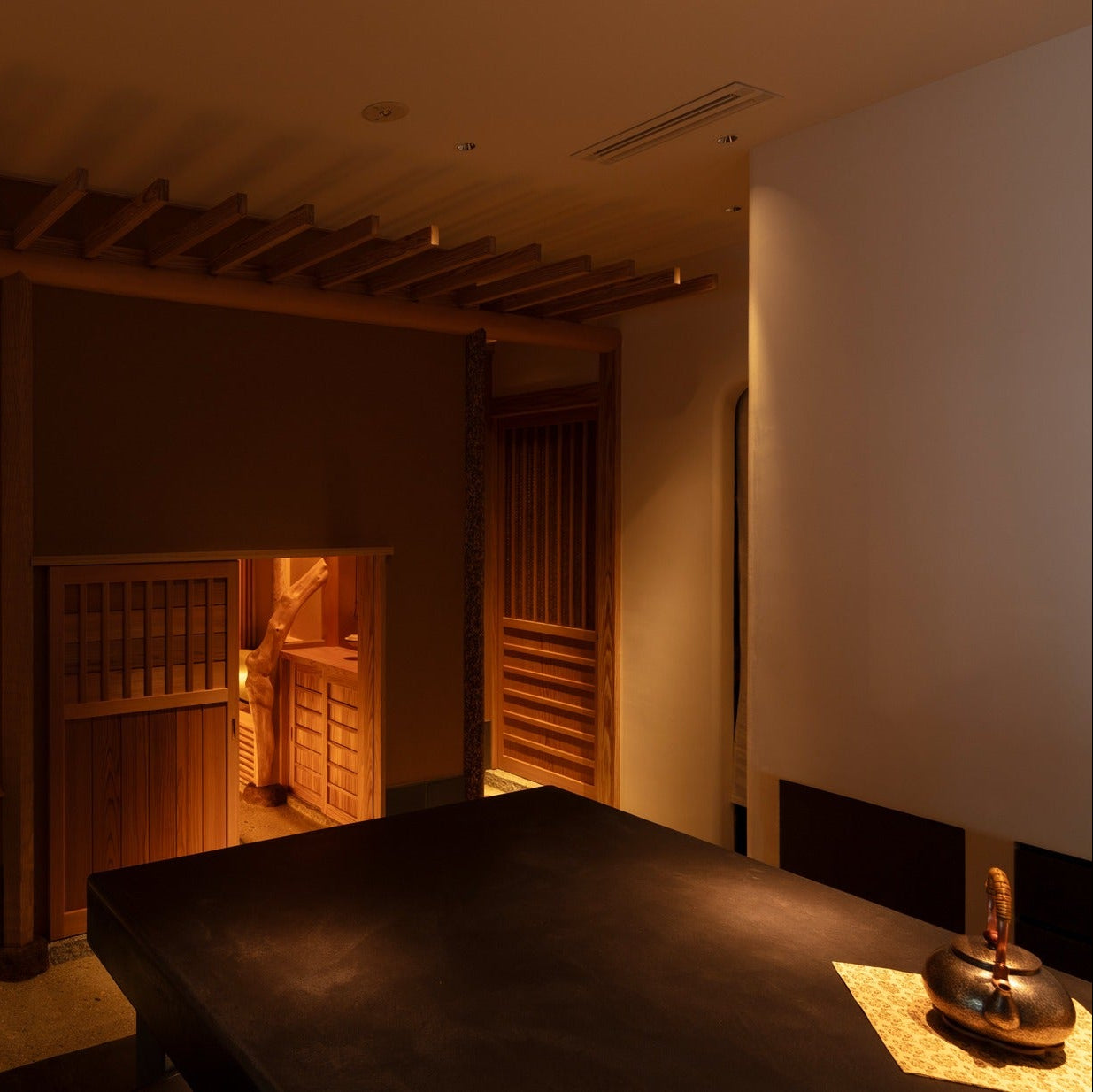 A cedar door stands open between the counter and an inner room of natural timber, layered Japanese architecture.