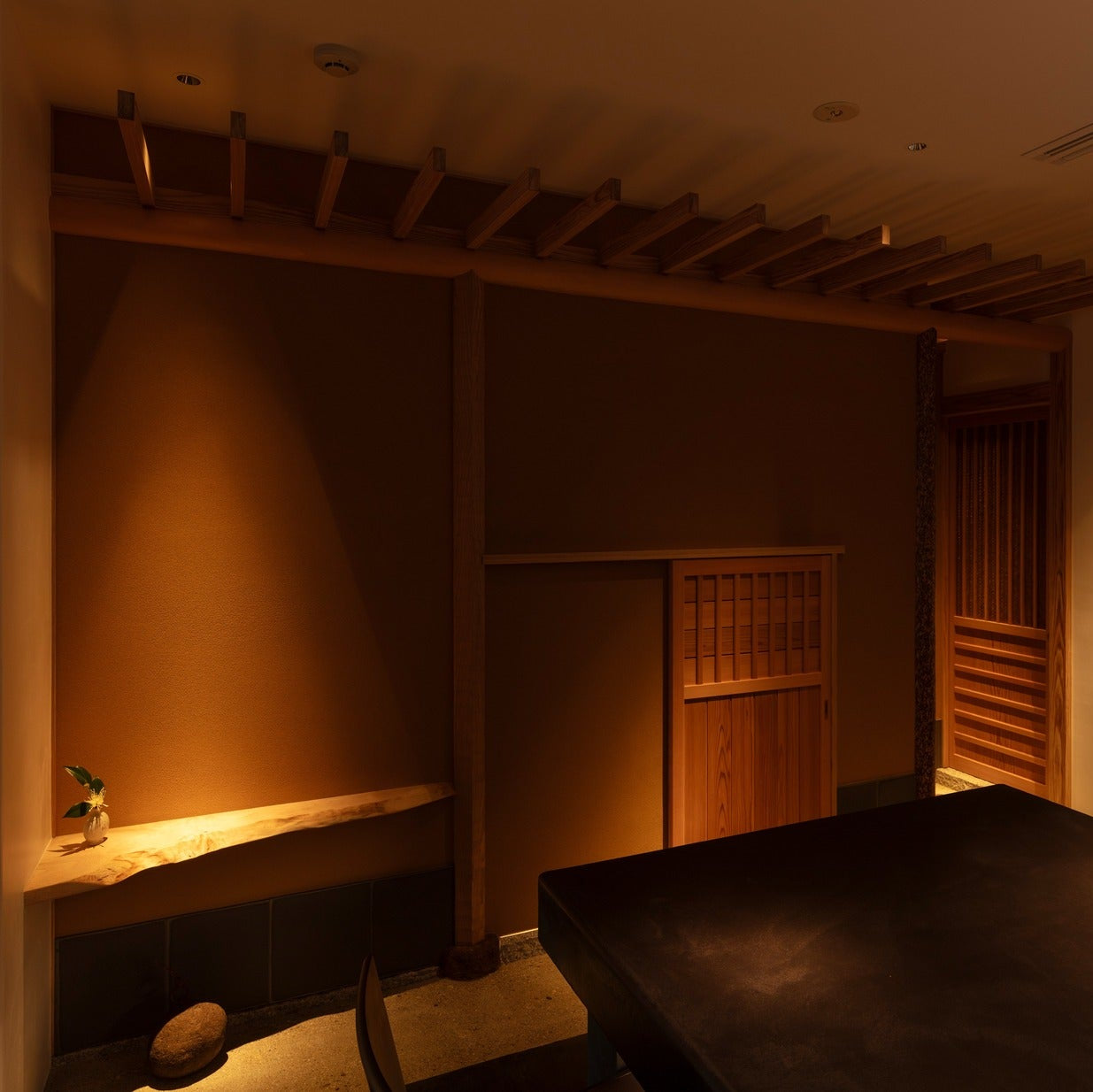 A live-edge japanese styleshelf holds a single sprig beside a closed cedar door 