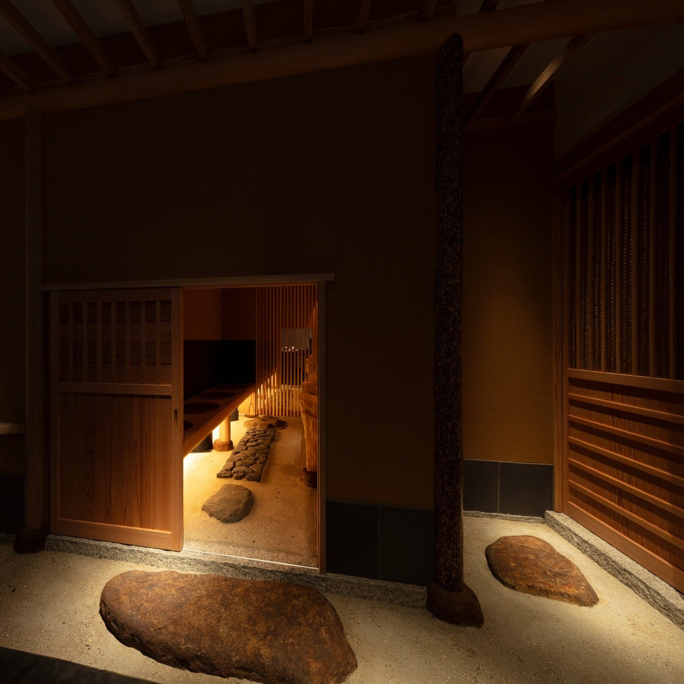 A sliding door shaped like a nijiriguchi opens to the chashitsu, stepping stones set in sand leading in.