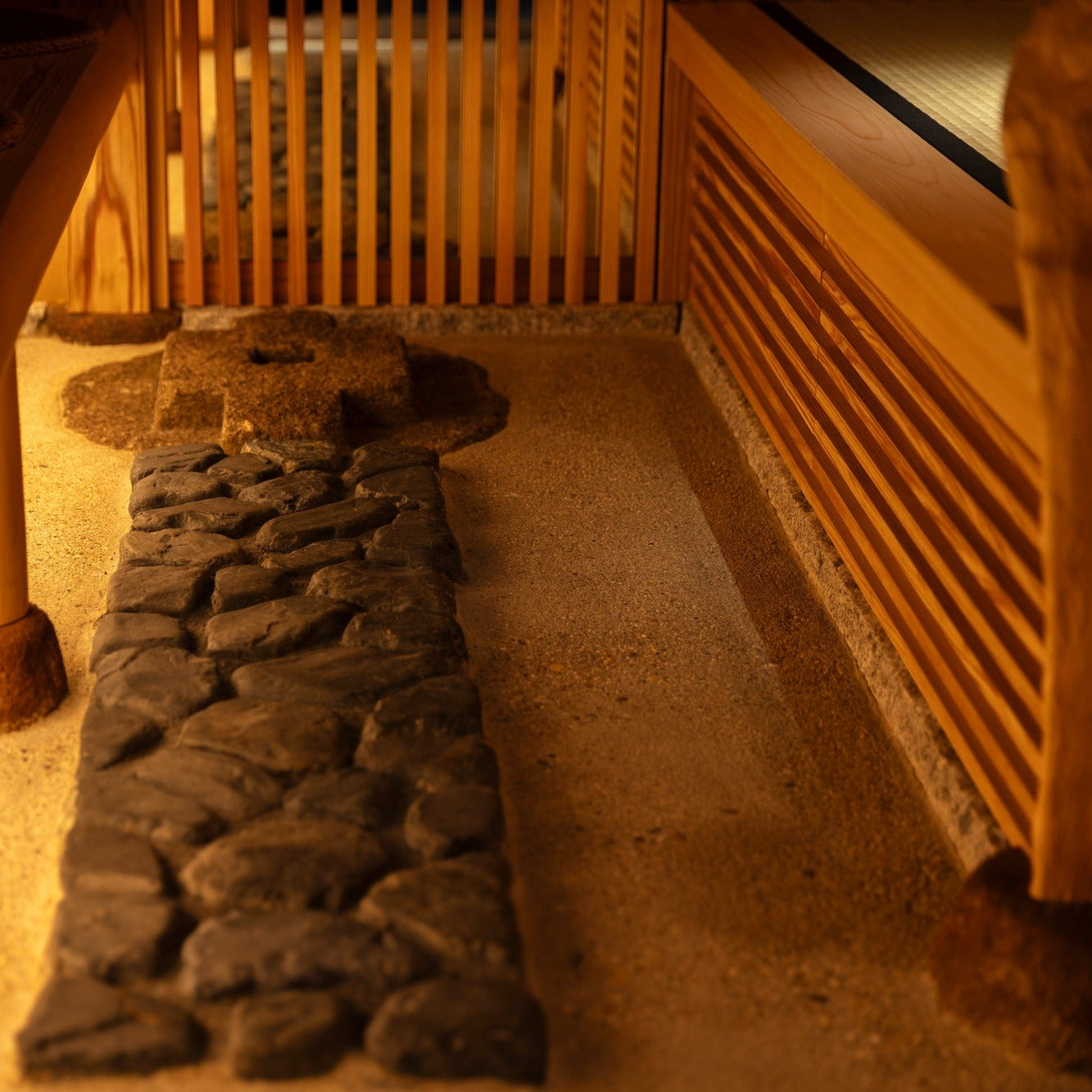 Detail of a cobblestone strip laid like a dry stream through pale sand, lit warmly from the side.