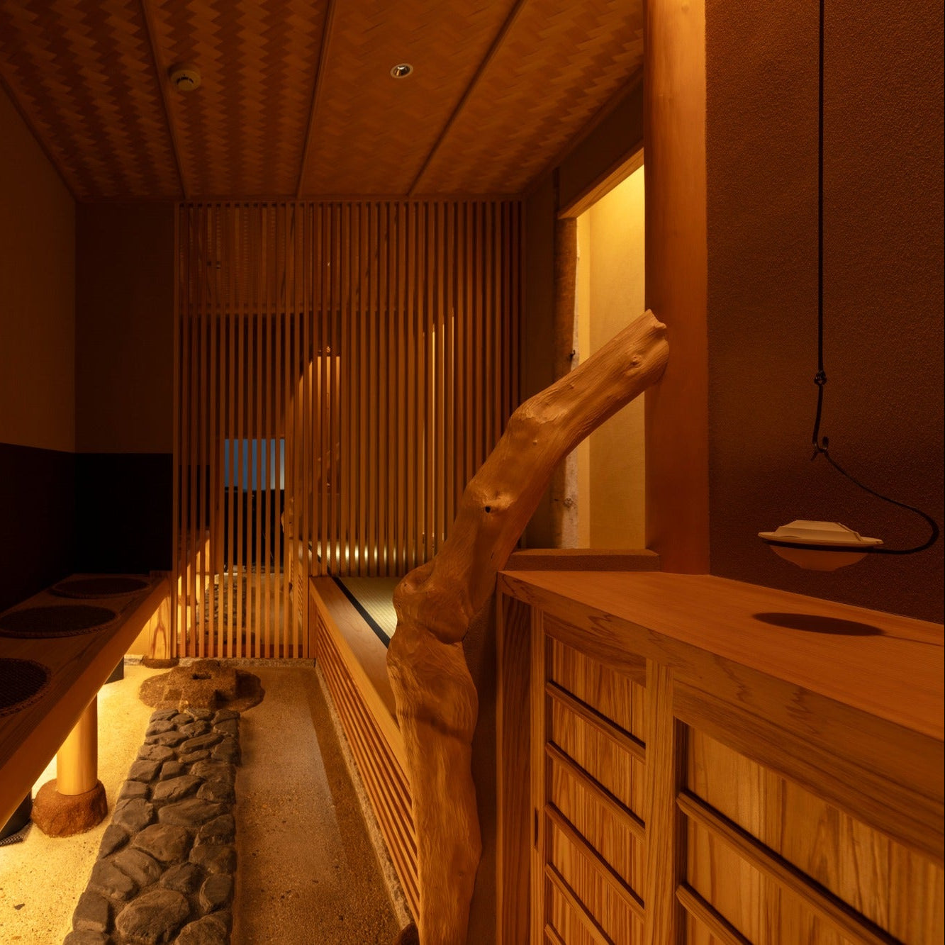 Inside the chashitsu, a long timber bench with round cushions faces a sand-and-stone channel beneath a woven bamboo ceiling.