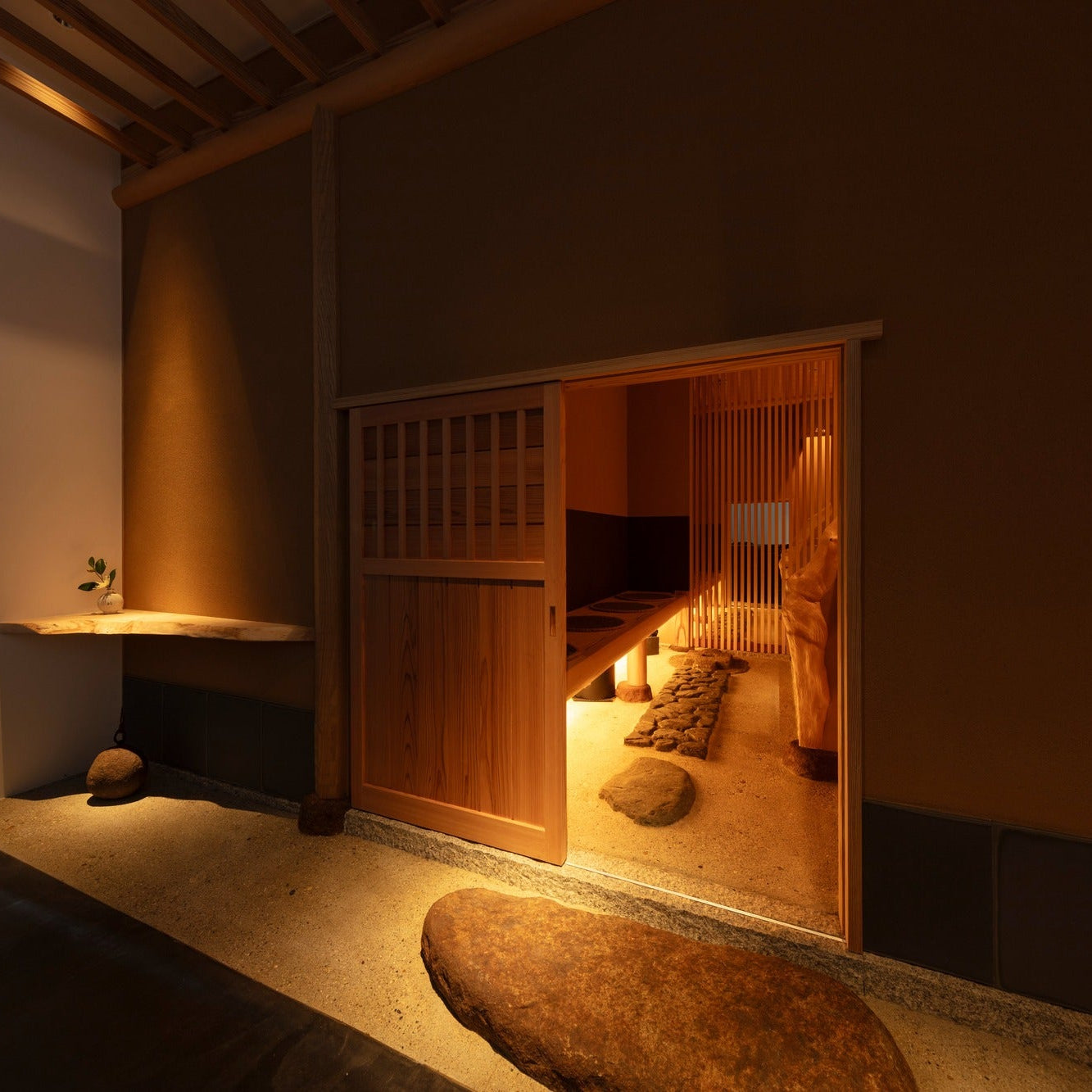 A cedar sliding door opens to a hidden tea room, stepping stones crossing a bed of sand in quiet Japanese architecture.
