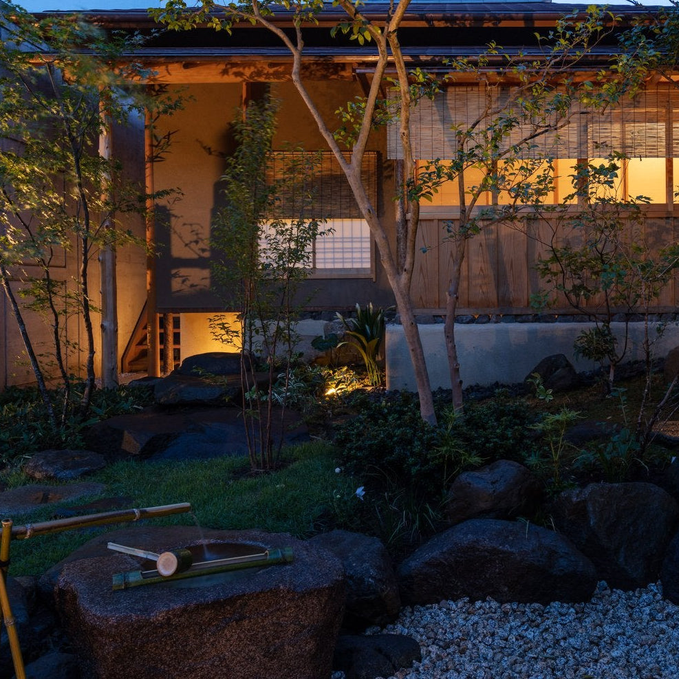 Chashitsu lit at dusk with a stone tsukubai water basin in the garden, Japanese tea house architecture in Tokyo.