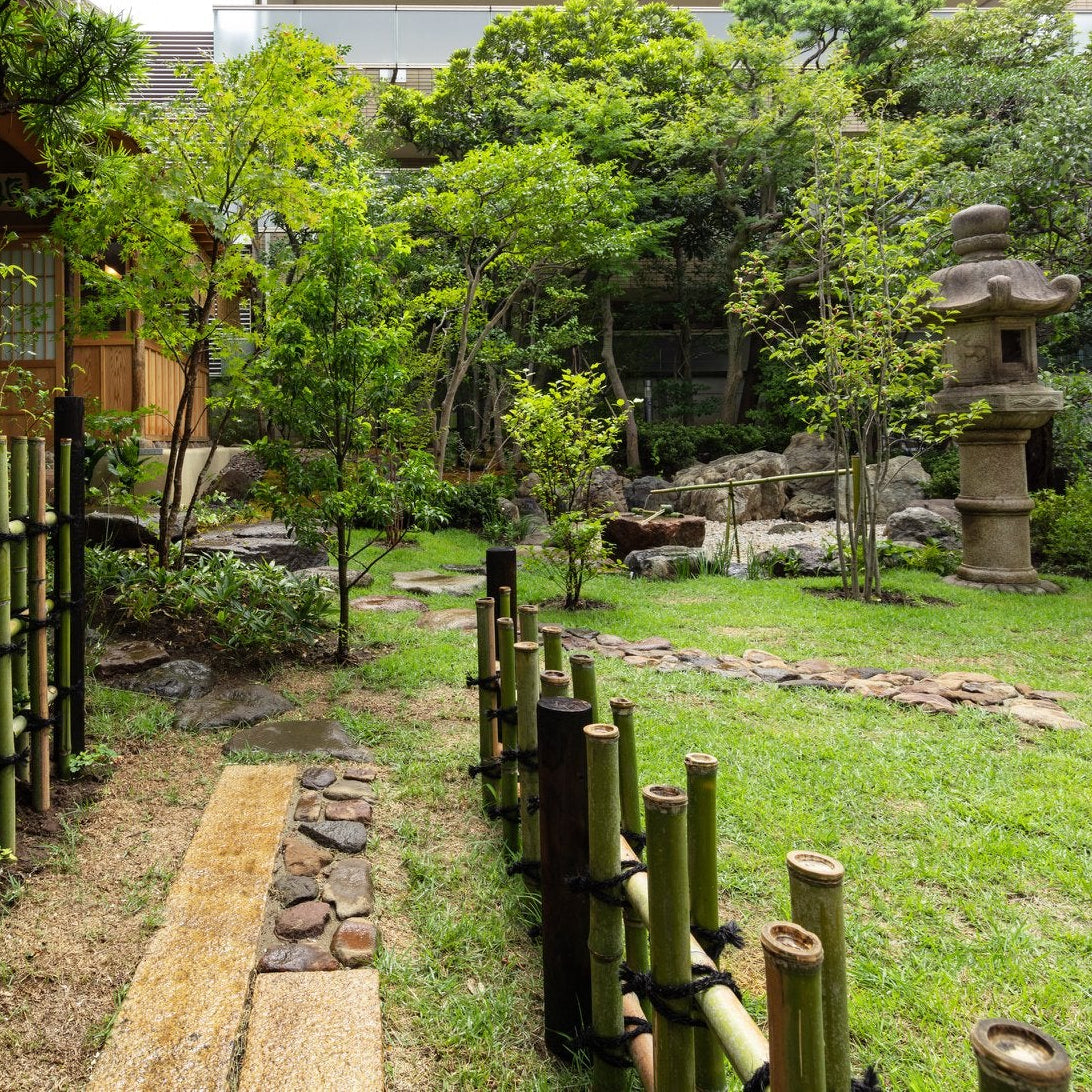 Japanese garden with a bamboo fence, pine, stone lantern and stepping-stone path beside a Roppongi chashitsu.