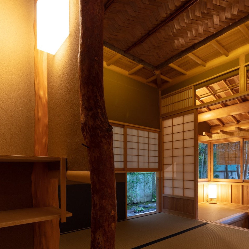 Tatami tea room at night with a natural log post and paper andon lamps, traditional chashitsu architecture.