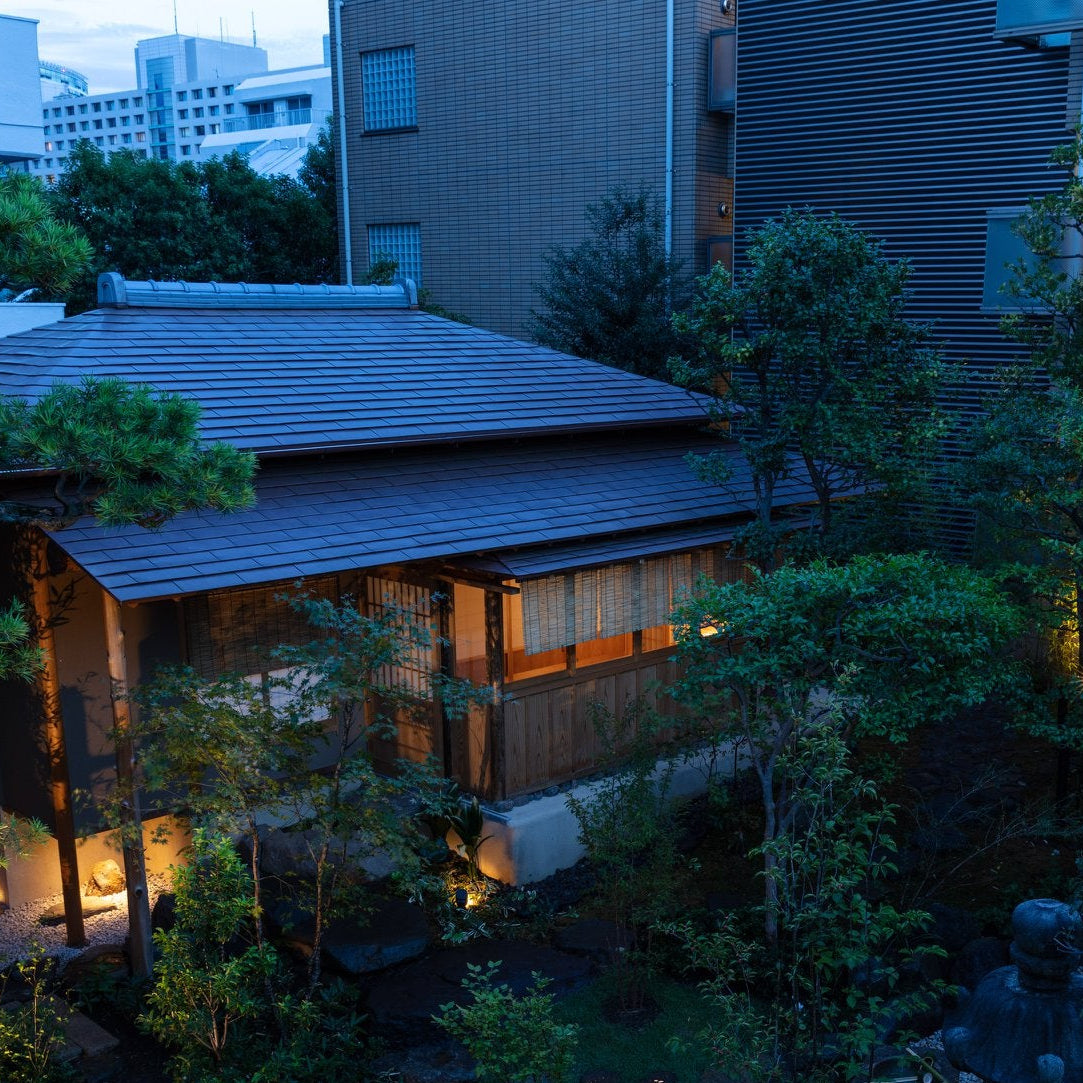 Tile-roofed Japanese tea house glowing at dusk within a city garden, Japanese architecture in Roppongi, Tokyo.