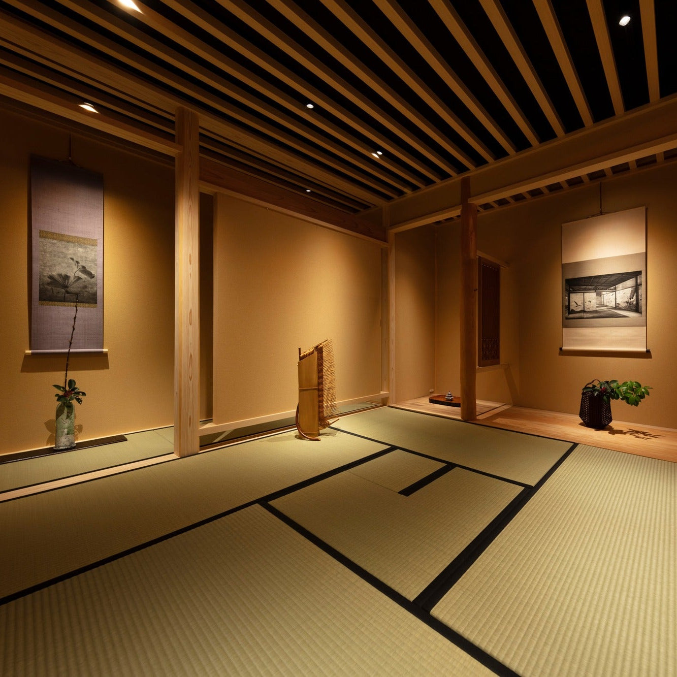 Tatami tea room with hanging scrolls and a bamboo artwork between cedar posts, a warm Japanese interior.