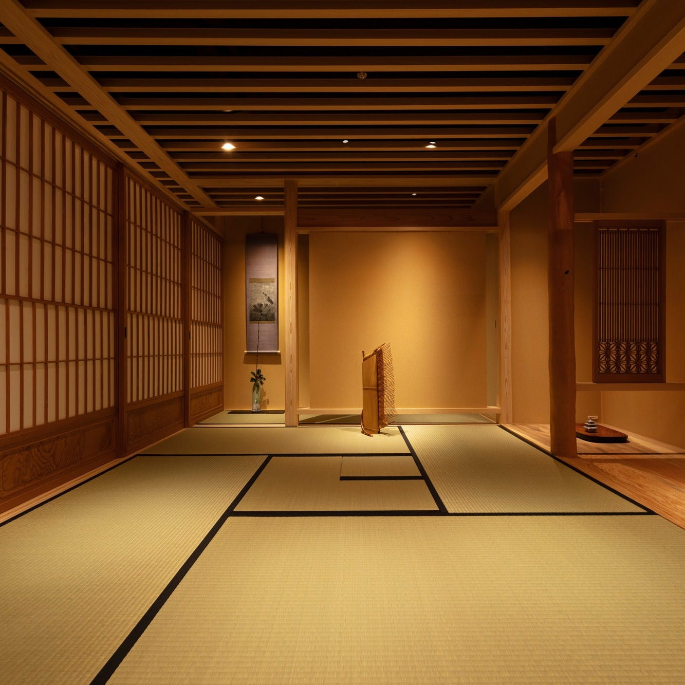Wide tatami chashitsu with a shoji wall and a small lounge beyond, hanging scrolls and cedar posts.