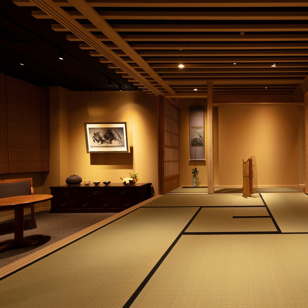 Tatami room with a framed ink work on an antique chest and hanging scrolls, a quiet Japanese interior.