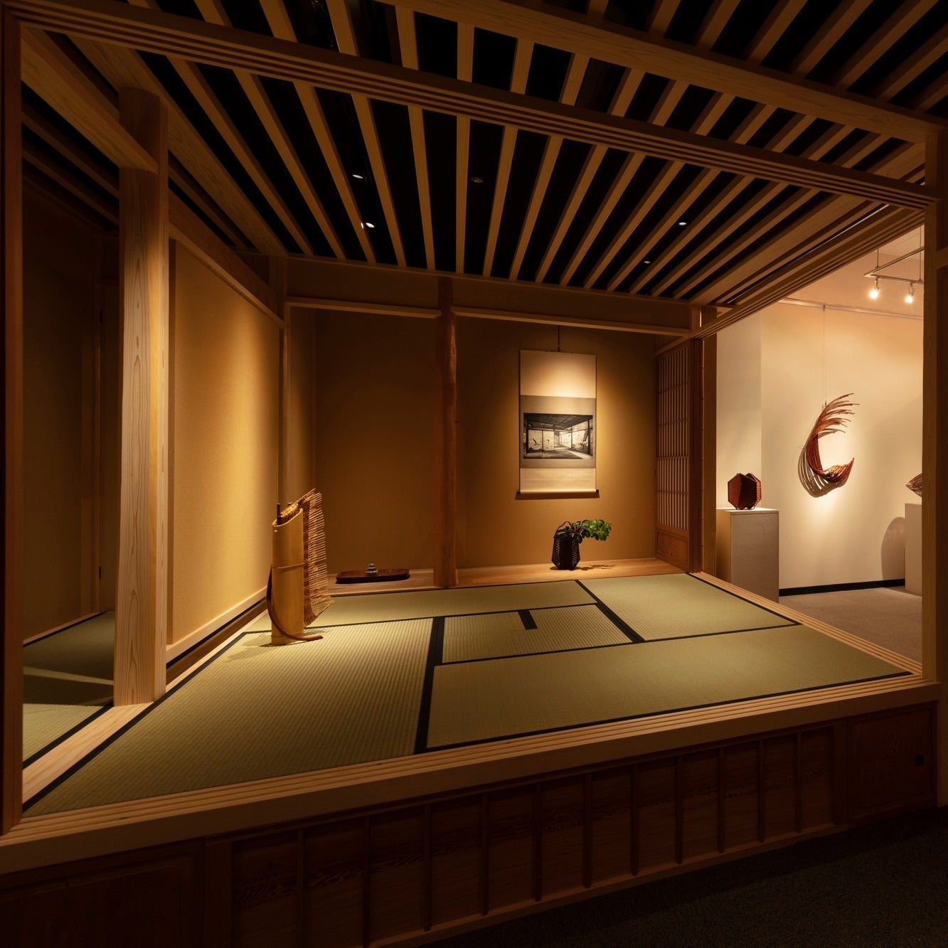 Raised tatami tea room beside a gallery wall holding a crescent-shaped bamboo sculpture, contemporary Japanese architecture.