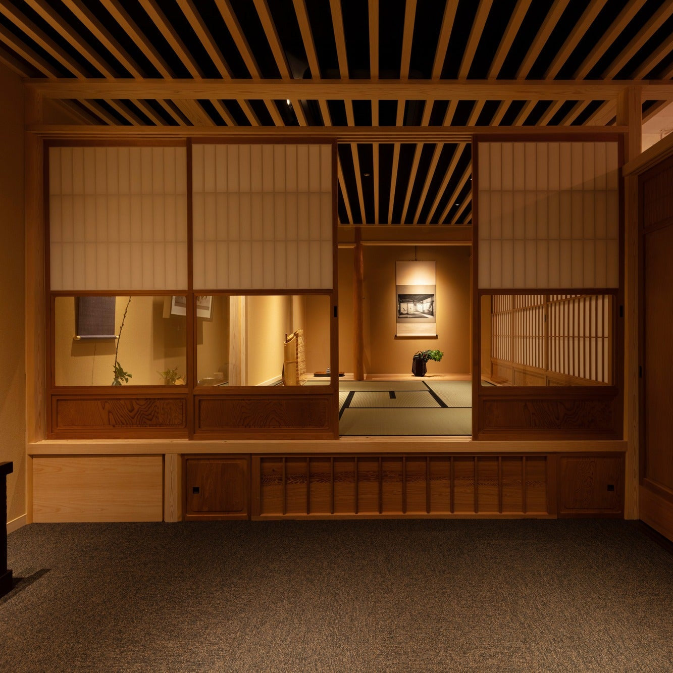 Symmetrical frontal view into a chashitsu through its shoji opening, a black-and-white scroll centred at the rear.