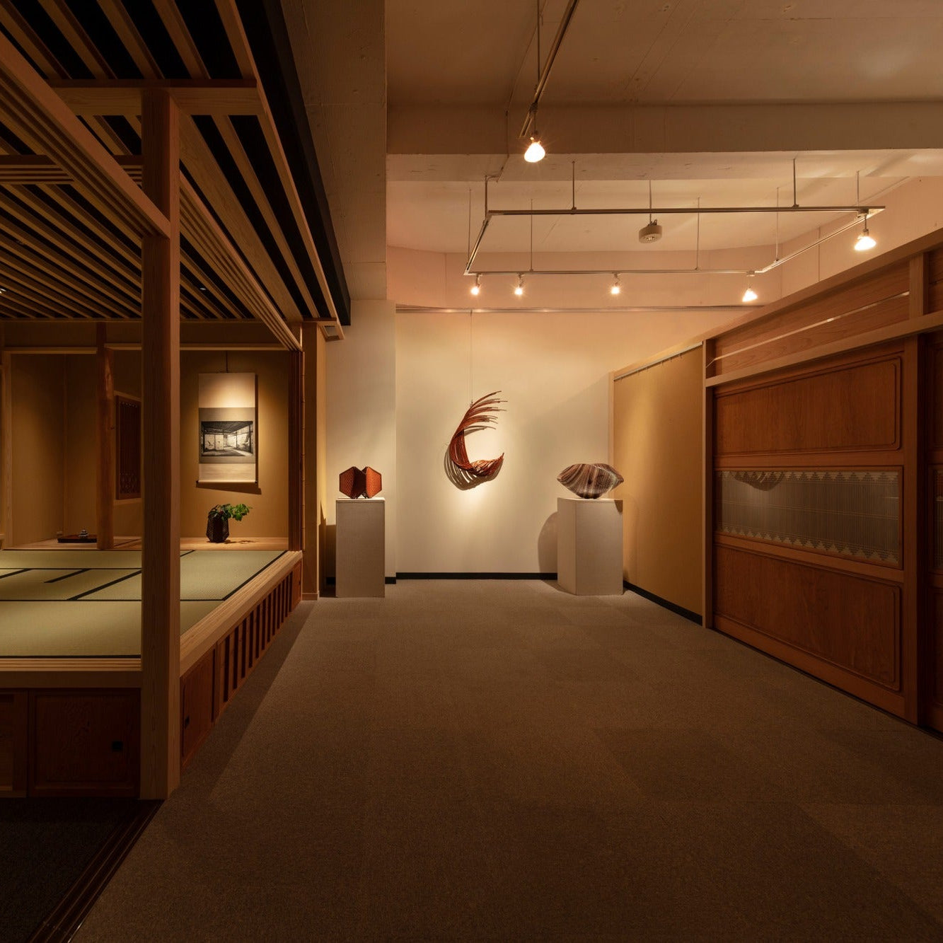 Angled view of a tea room and gallery with bamboo and ceramic art on pedestals and wooden display cabinets.