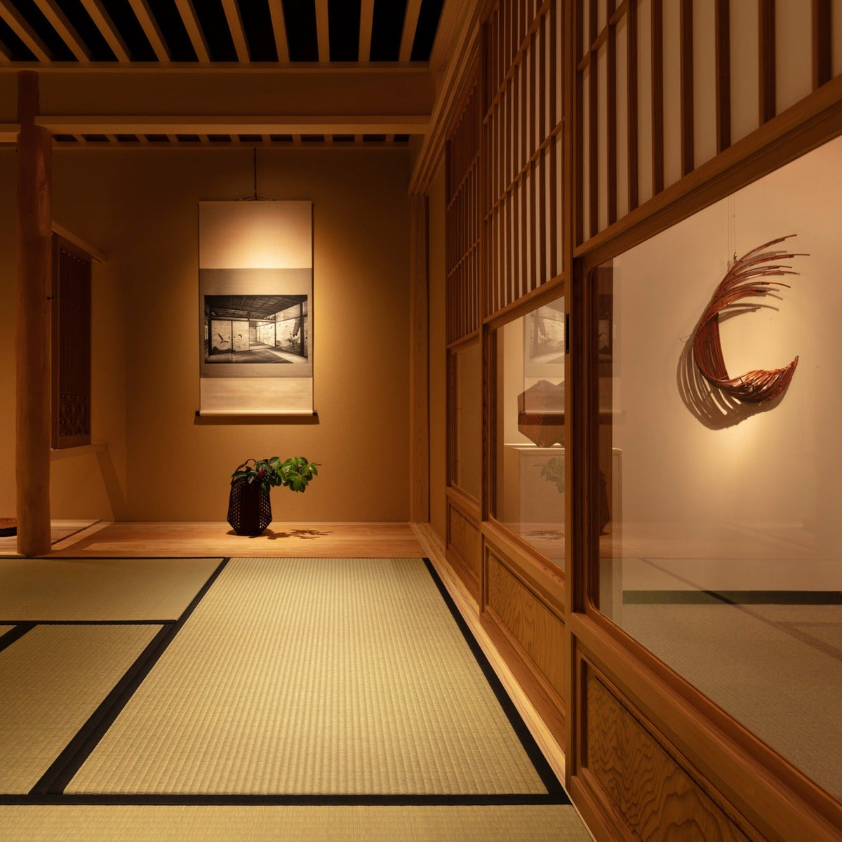 Tea room corner with a black-and-white photographic scroll and a bamboo crescent artwork seen through glass shoji.