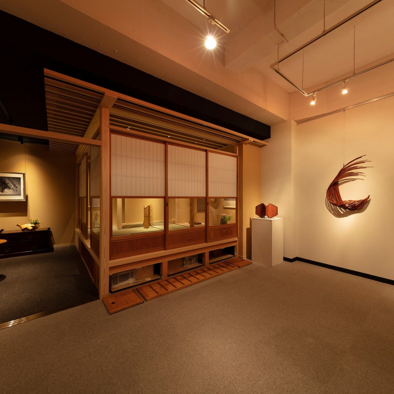 Tea room with shoji partly open beside a gallery wall holding a bamboo crescent sculpture.