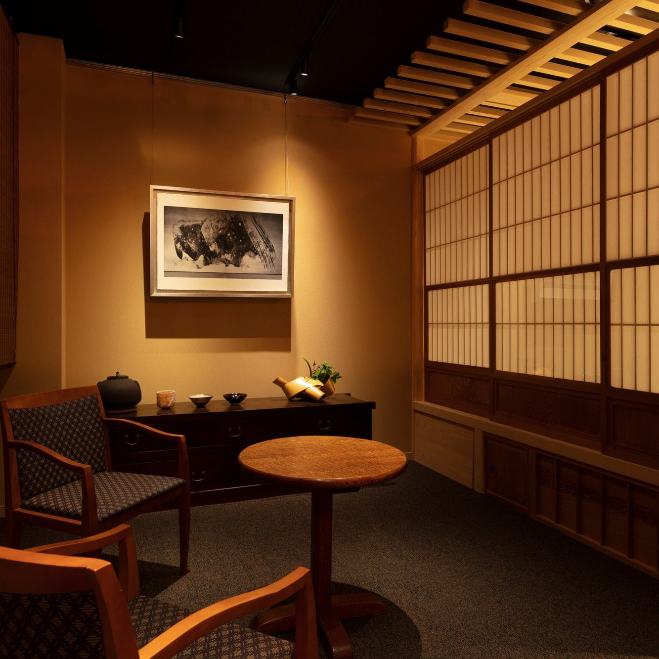 Waiting area with armchairs, reed blinds and tea utensils on an antique chest beside a tea room, a calm Japanese interior in a Ginza gallery.