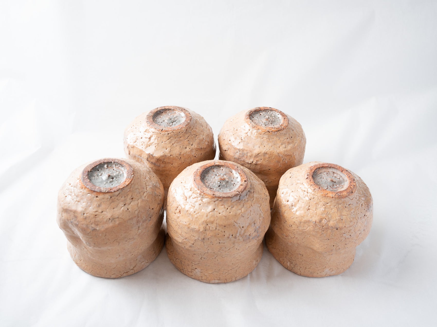 All five ceramic cups turned upside down together, showcasing the unique, dynamic crawled glaze runs and rustic exposed clay around each circular foot.