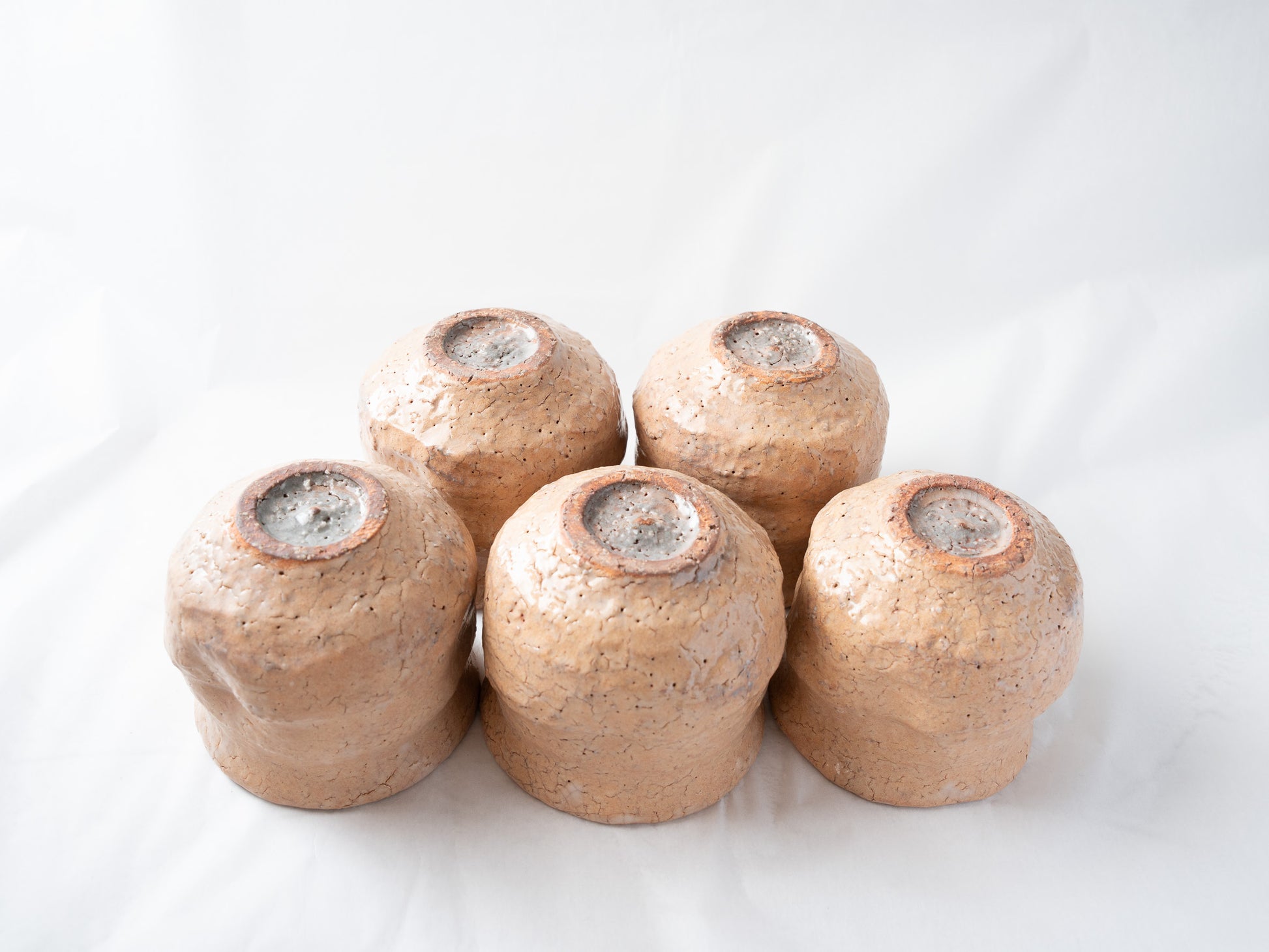 All five ceramic cups turned upside down together, showcasing the unique, dynamic crawled glaze runs and rustic exposed clay around each circular foot.