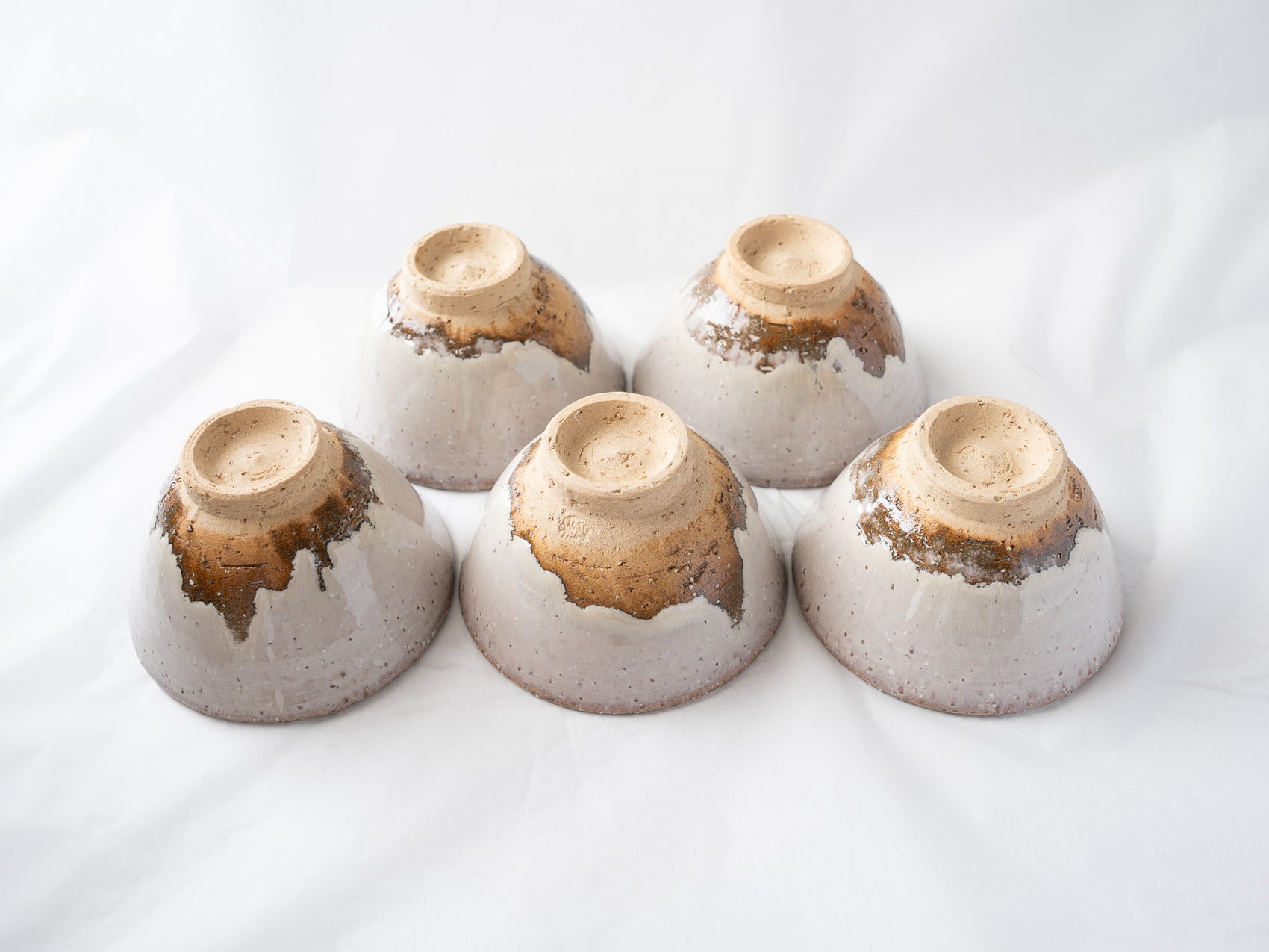 The five Hagiyaki cups turned upside down, showcasing the dramatic contrast between the flowing white glaze and the unglazed orange-brown clay bases.