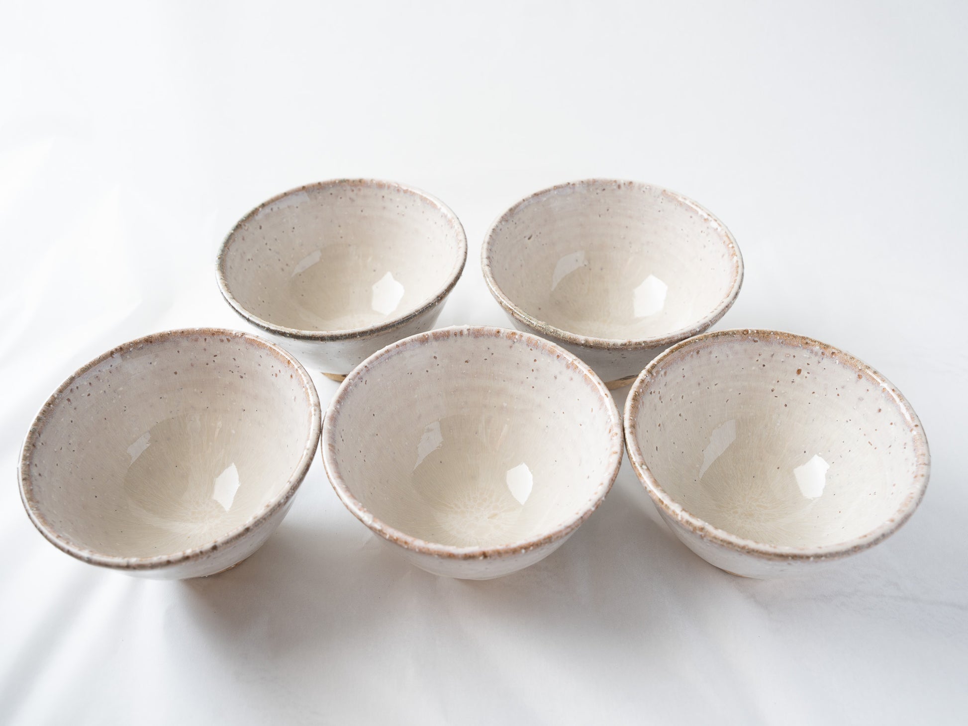 Overhead view of five Hagiyaki Kumidashi cups arranged in a crescent layout, displaying the unique variations of iron spots and soft white glaze inside each bowl.