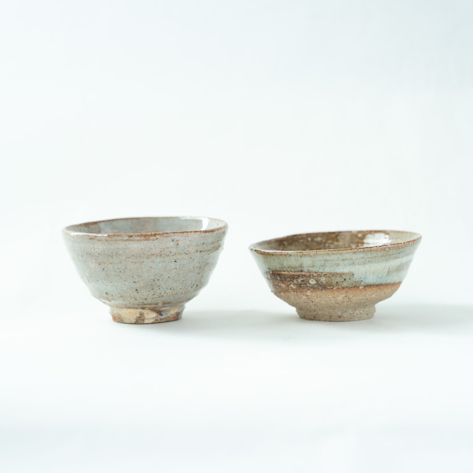 A slightly adjusted front shot of the two ceramic cups, highlighting the gentle asymmetry and organic rim lines of the hand-formed vessels.