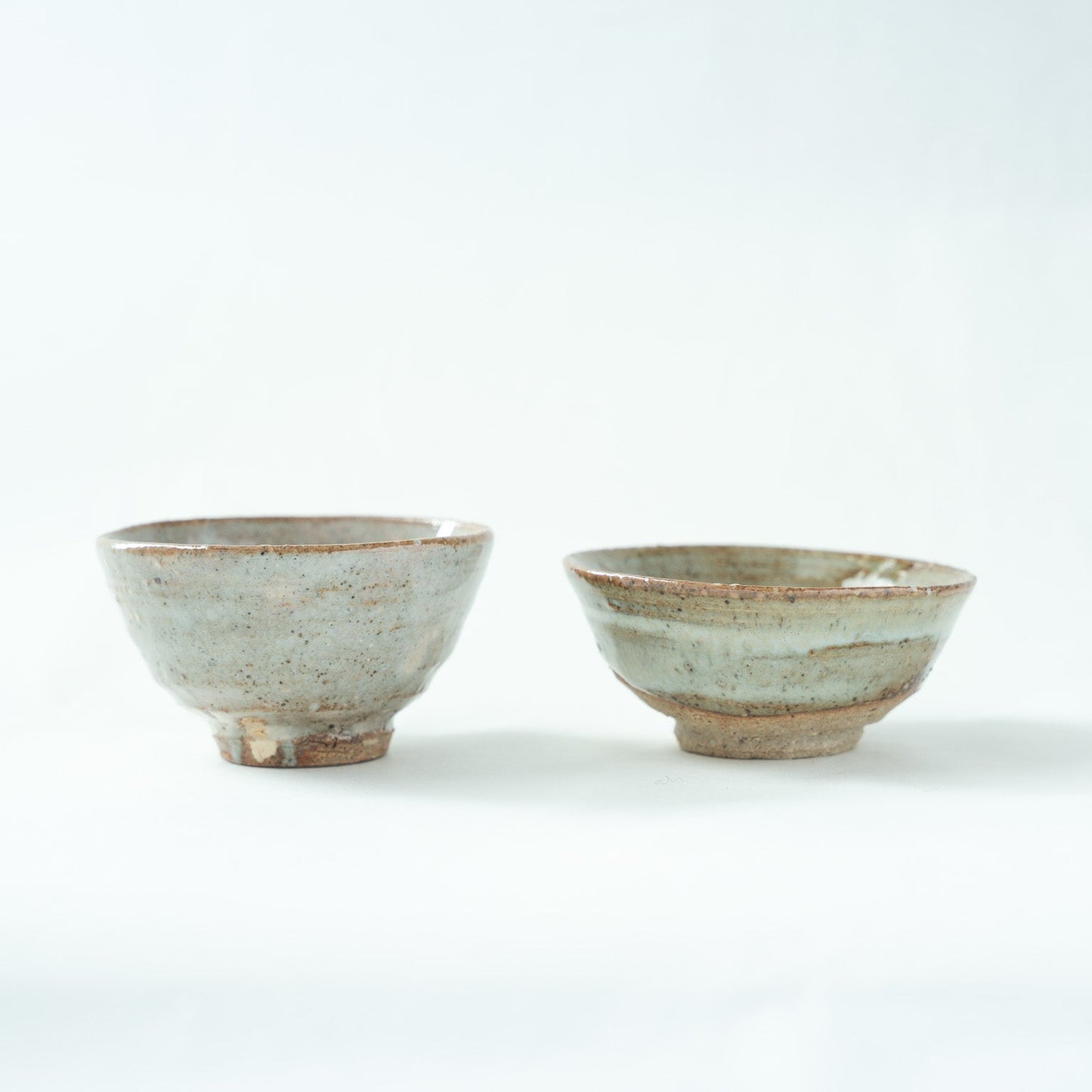 Side profile view of the set, capturing the subtle light reflections along the translucent glaze layers of both contemporary cups.