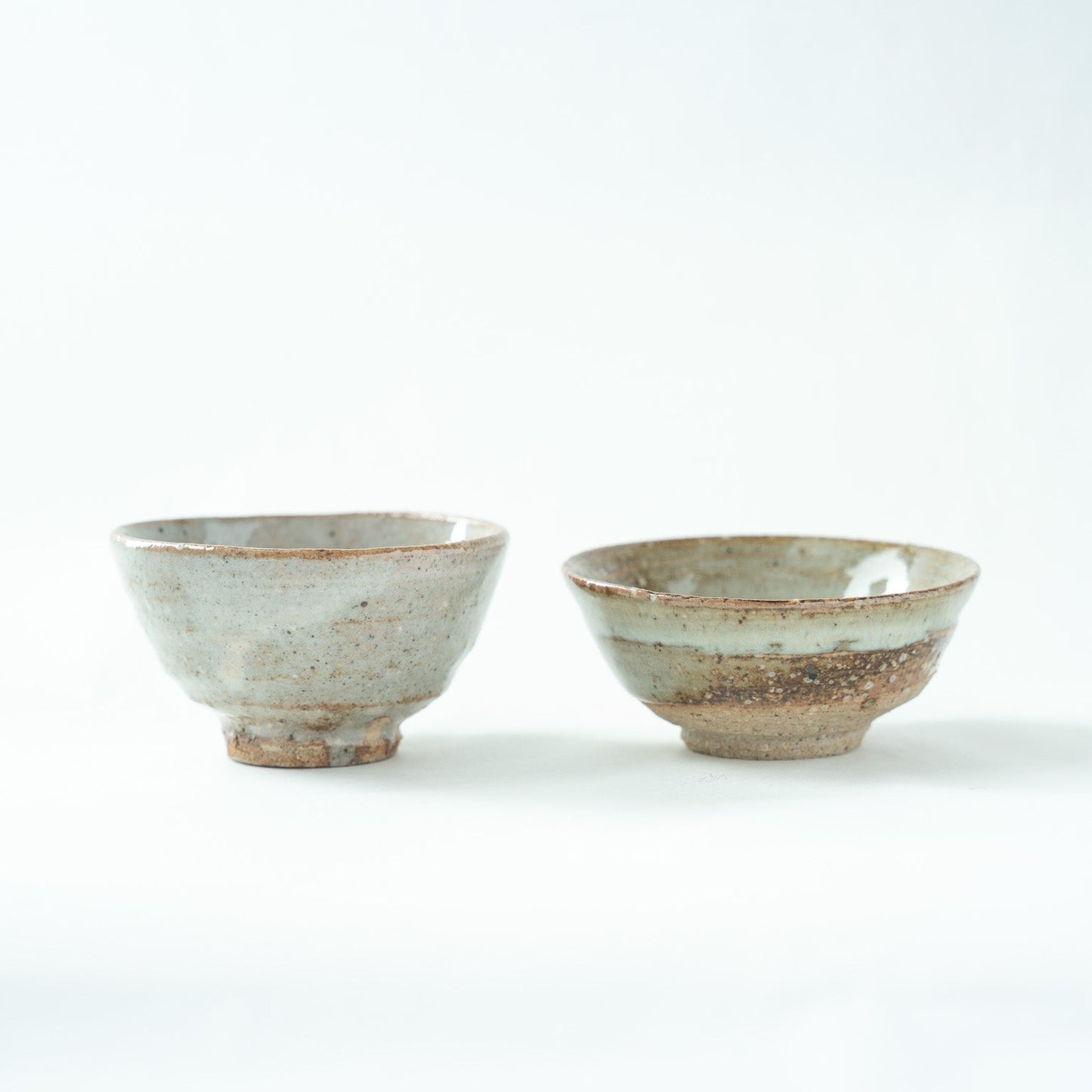 Rear view of the two Hajime Kato sake cups, showcasing the fine iron speckles on the left vessel and the rustic clay surface near the base of the right bowl.