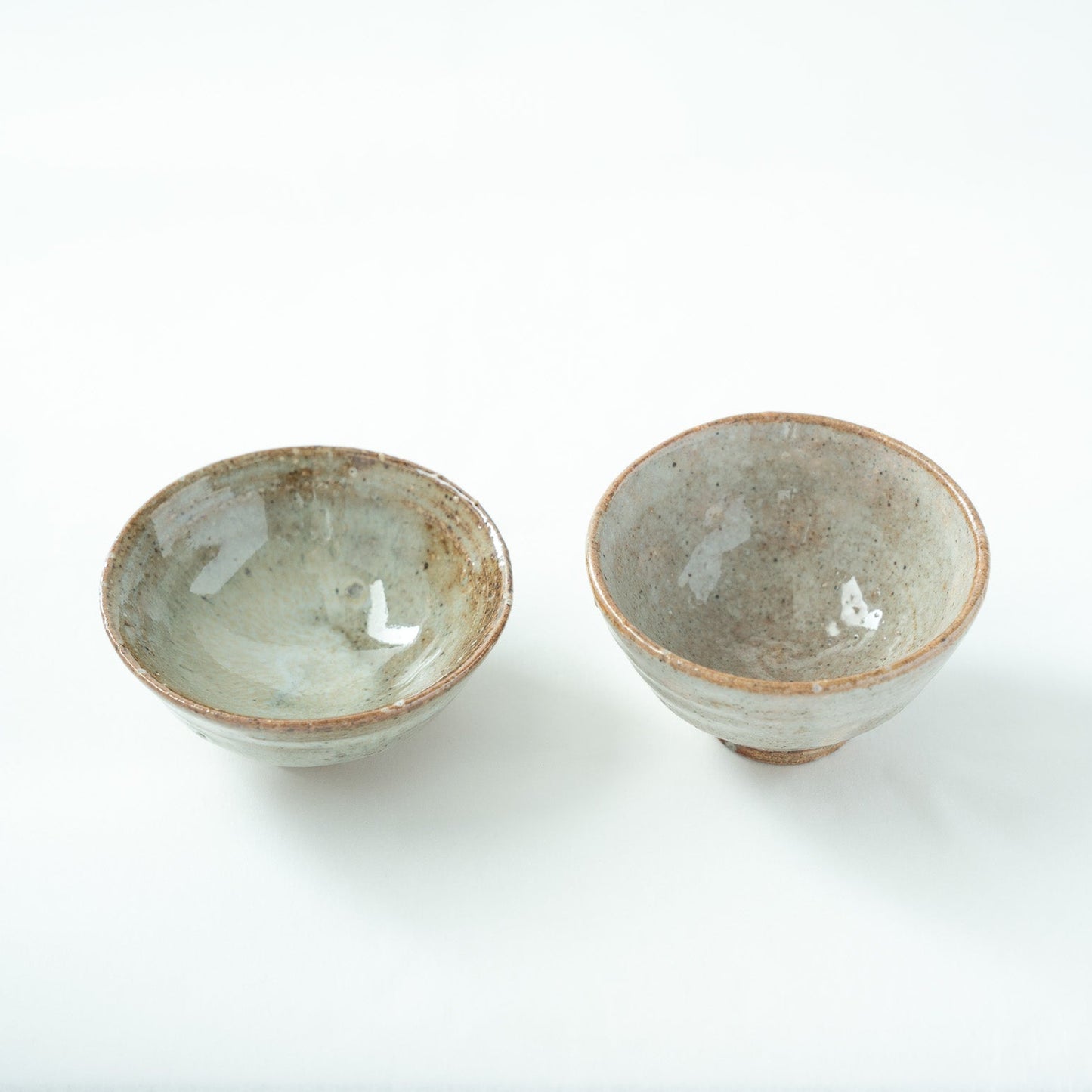 Close-up top view looking inside the bowls, emphasizing the fine crackles and calm pool of glaze at the bottom of the vessels.