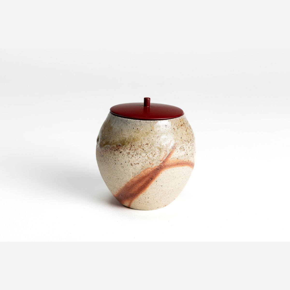 Front view of the small rounded Bizen tea caddy with its red lacquered lid, the orange straw marks running diagonally across the sandy body.