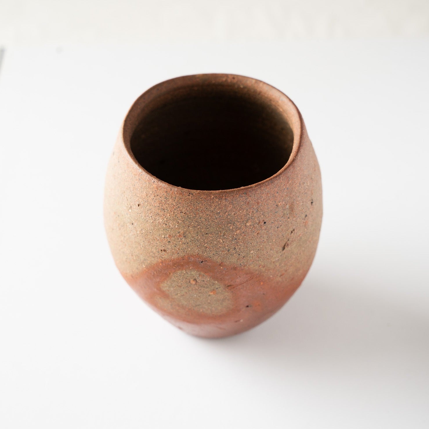 High-angle view of a rounded, unglazed ceramic YUNOMI cup by Hiroshi Goseki, showcasing a circular reddish fire-mark against a textured brown body.
