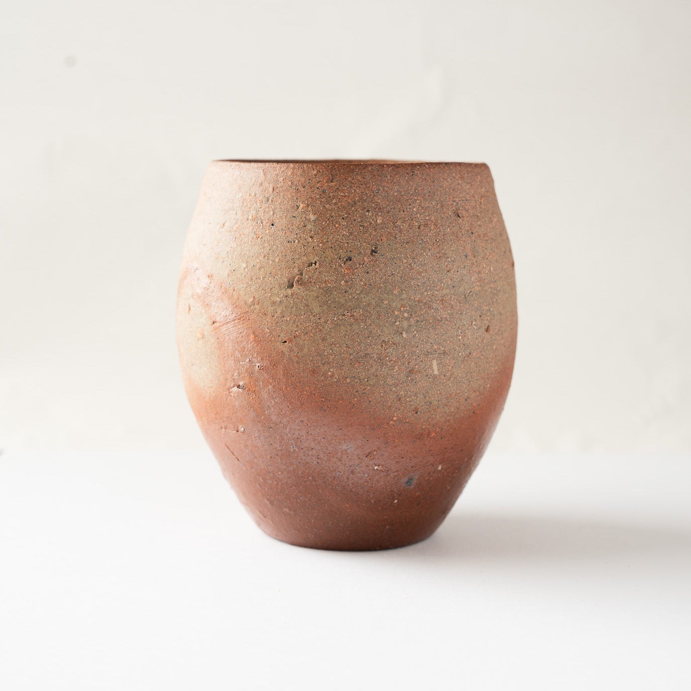 Front profile of the egg-shaped unglazed ceramic cup, emphasizing its clean swelling form and earthy kiln-fired surface transitions.