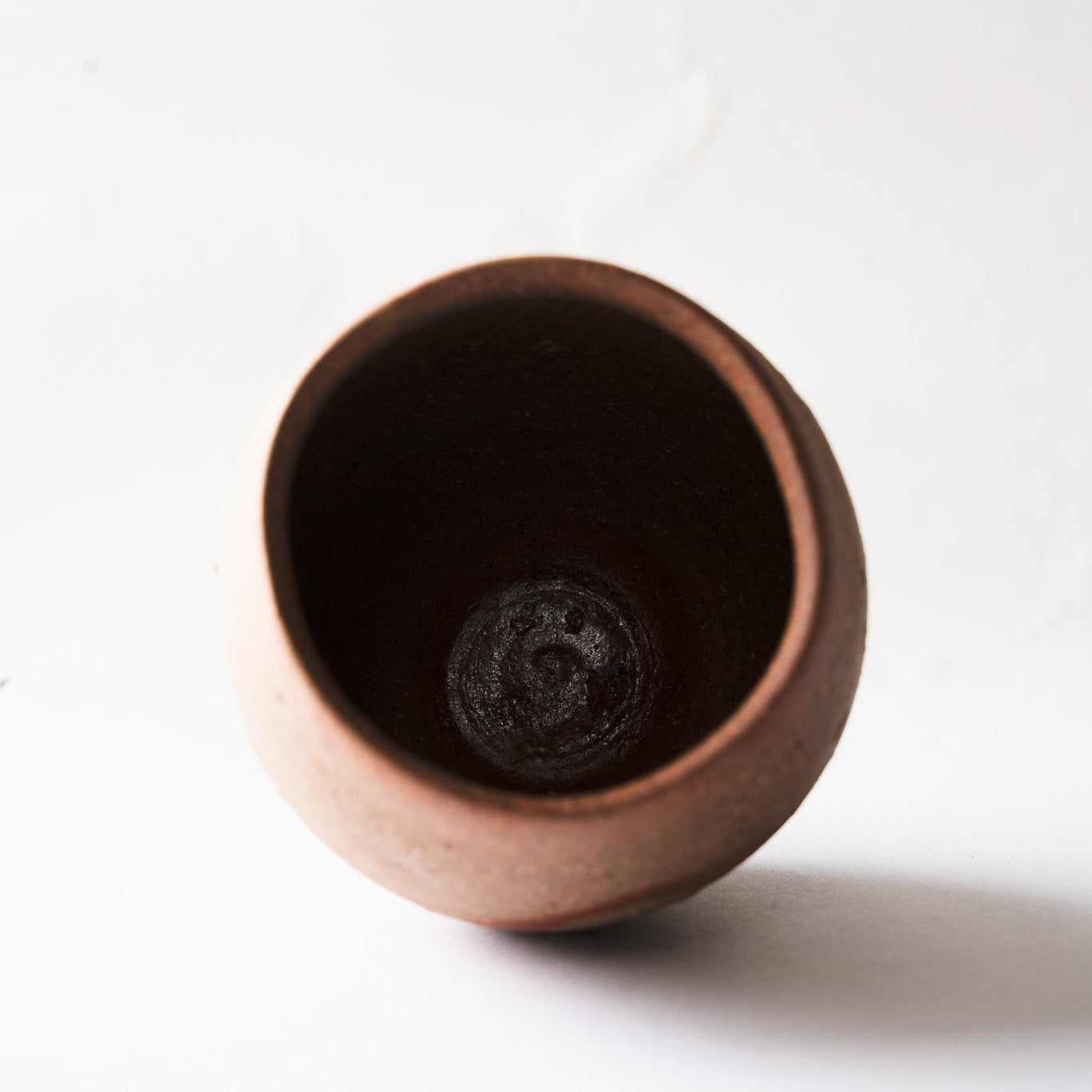 Top-down view into the deep, dark interior of the rounded YUNOMI cup, revealing the spiraling throwing lines at the interior base.