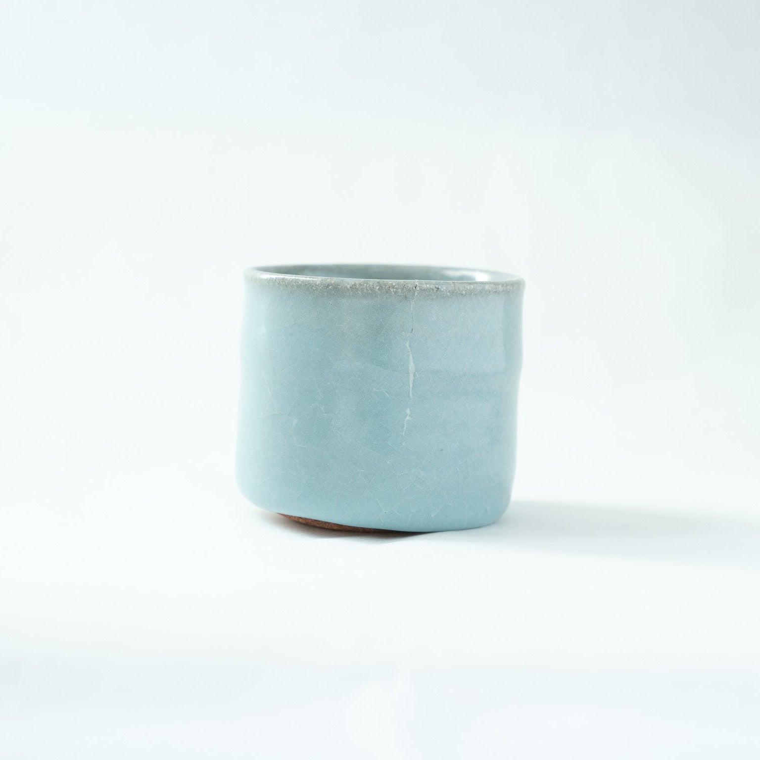 Another side profile view, displaying a vertical crackle line extending from the rim down the exterior wall of the celadon cup.