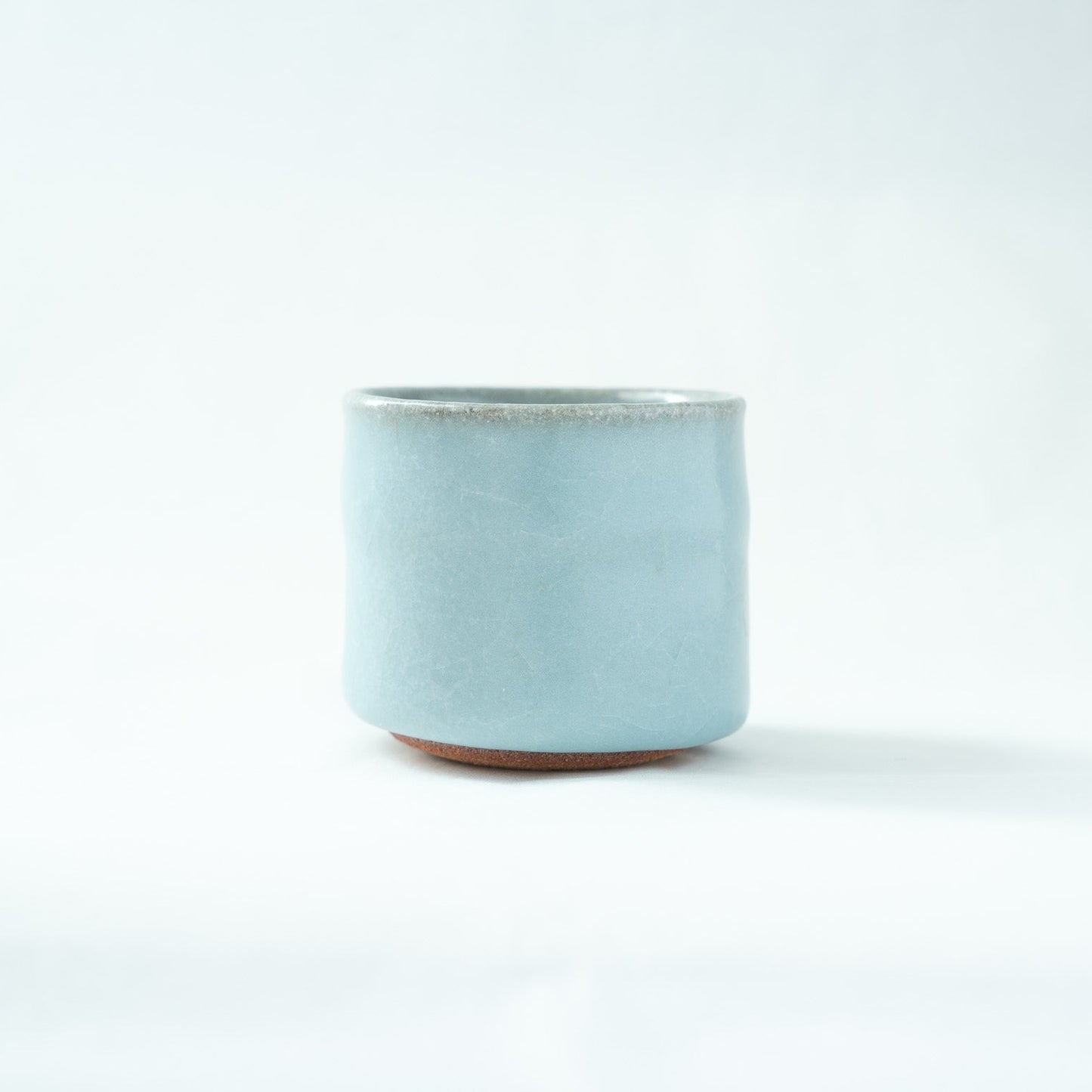 Front view of the cylindrical celadon GUINOMI by Hiroshi Nakajima, showing a soft, misty sky-blue glaze with a rustic clay base subtly visible at the bottom.