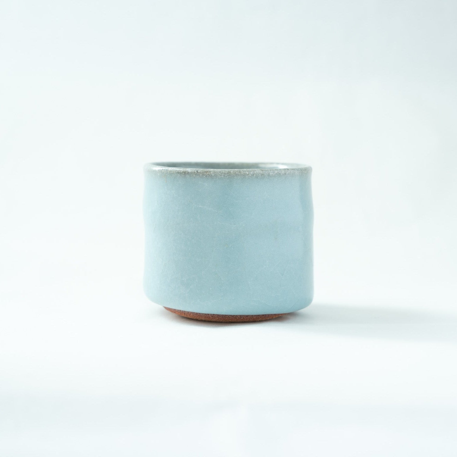 Front view of the cylindrical celadon GUINOMI by Hiroshi Nakajima, showing a soft, misty sky-blue glaze with a rustic clay base subtly visible at the bottom.
