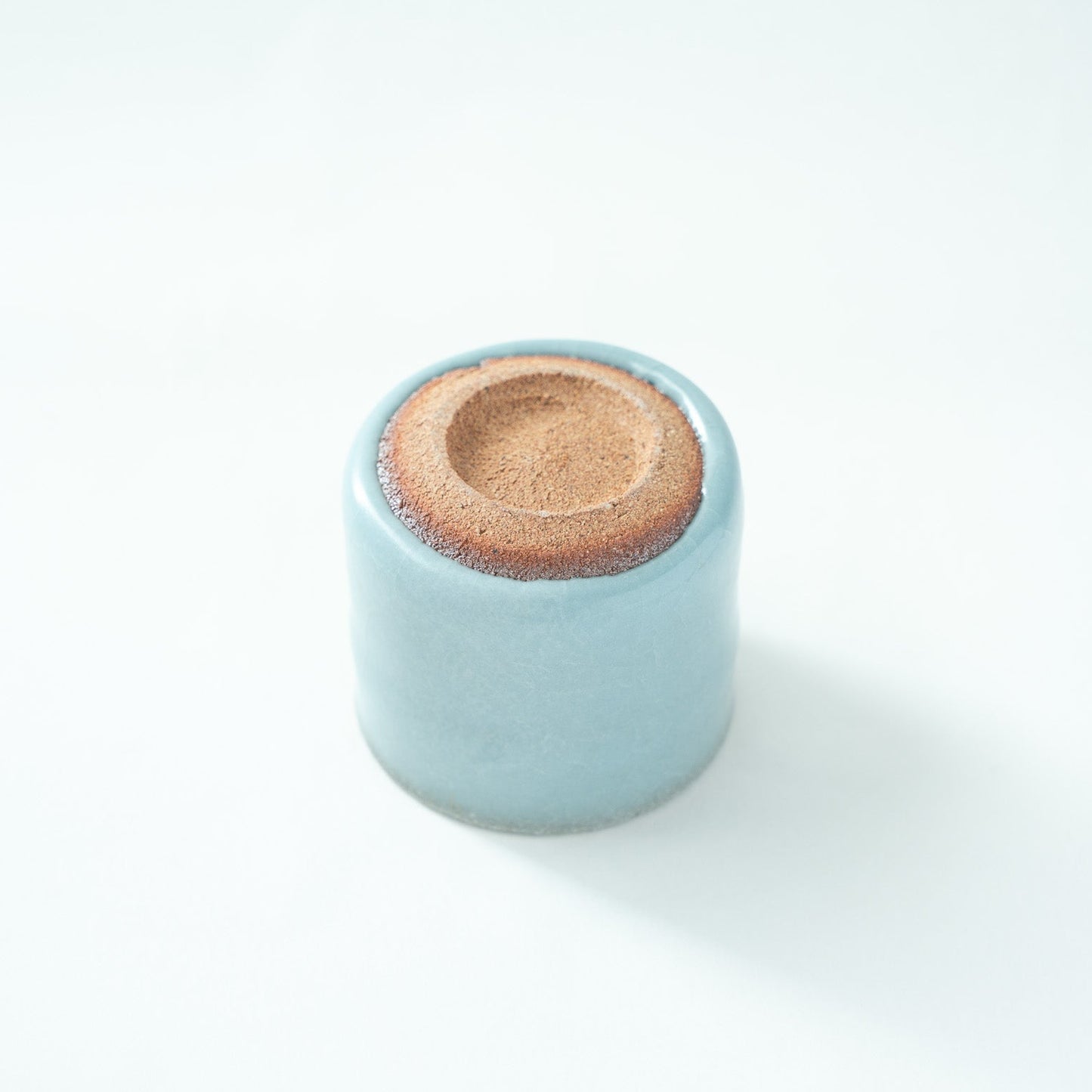 Inverted view of the celadon cup, revealing the rustic, unglazed reddish-brown pottery foot in sharp contrast with the refined blue glaze.