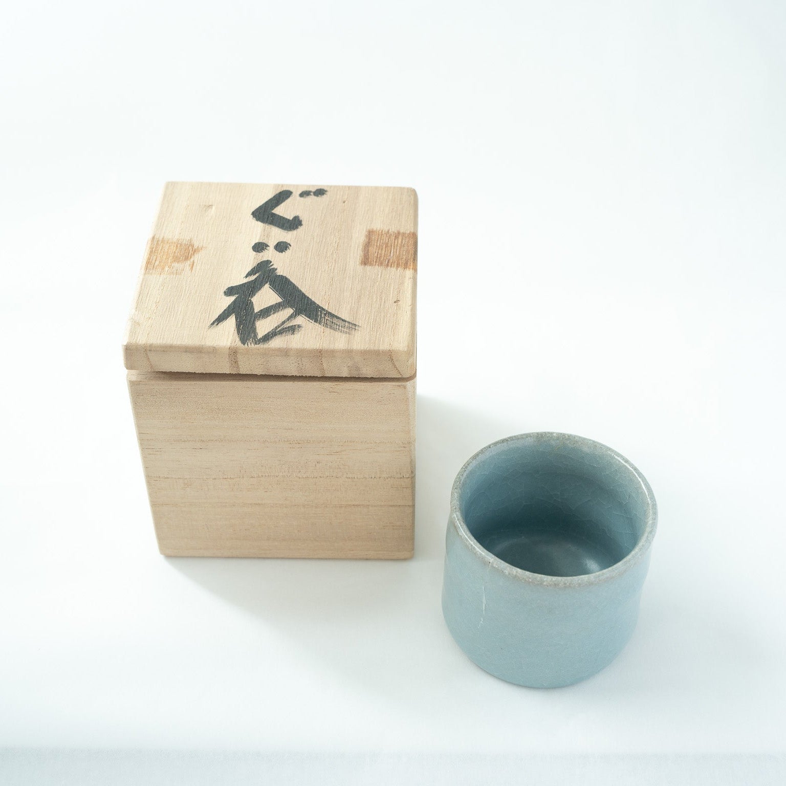 The sky-blue celadon GUINOMI presented next to its original signed wooden box with the calligraphy inscription "Guinomi" on the lid.