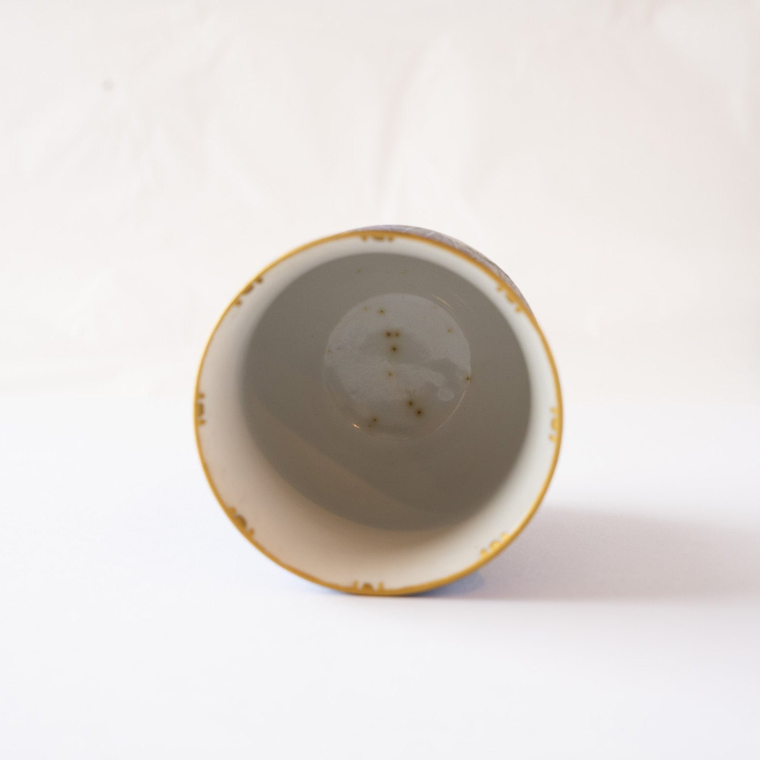 Direct top-down interior view of the YUNOMI cup, showing the smooth pale glaze with tiny natural iron spots settling at the bottom.