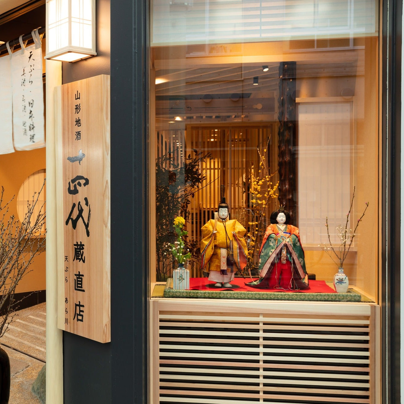 Facade detail with a noren curtain and a window display of seasonal dolls at a Japanese restaurant.
