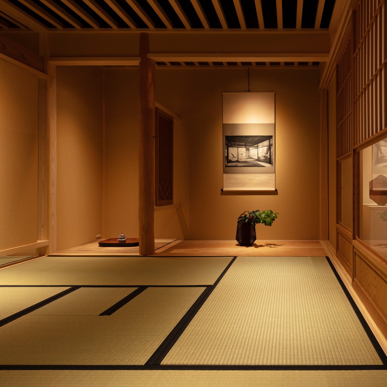 A serene traditional Japanese tearoom with warm lighting, featuring a tokonoma alcove with a hanging scroll, seasonal ikebana flower arrangement, and tatami mat flooring.