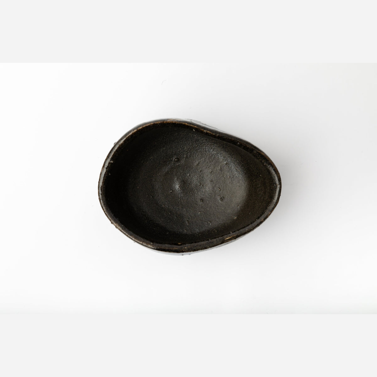 Vue plongeante à la verticale dans le bol : un fond sombre et lisse avec une flaque plus claire au centre, à l'intérieur de la lèvre ovale.