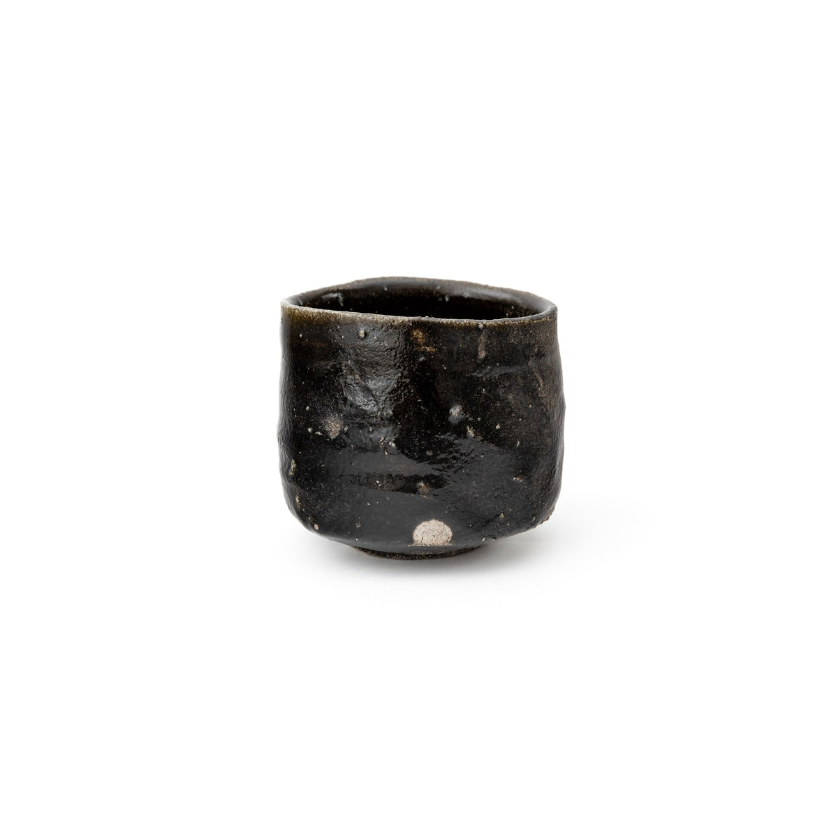 Front view of the small upright black tea bowl on white, the dry leaden sheen of the hikidashi glaze and a pale fleck near the foot.