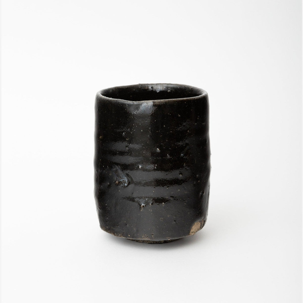 Front view of the tall black cylindrical tea cup on a white ground, the glossy glaze catching a vertical highlight.