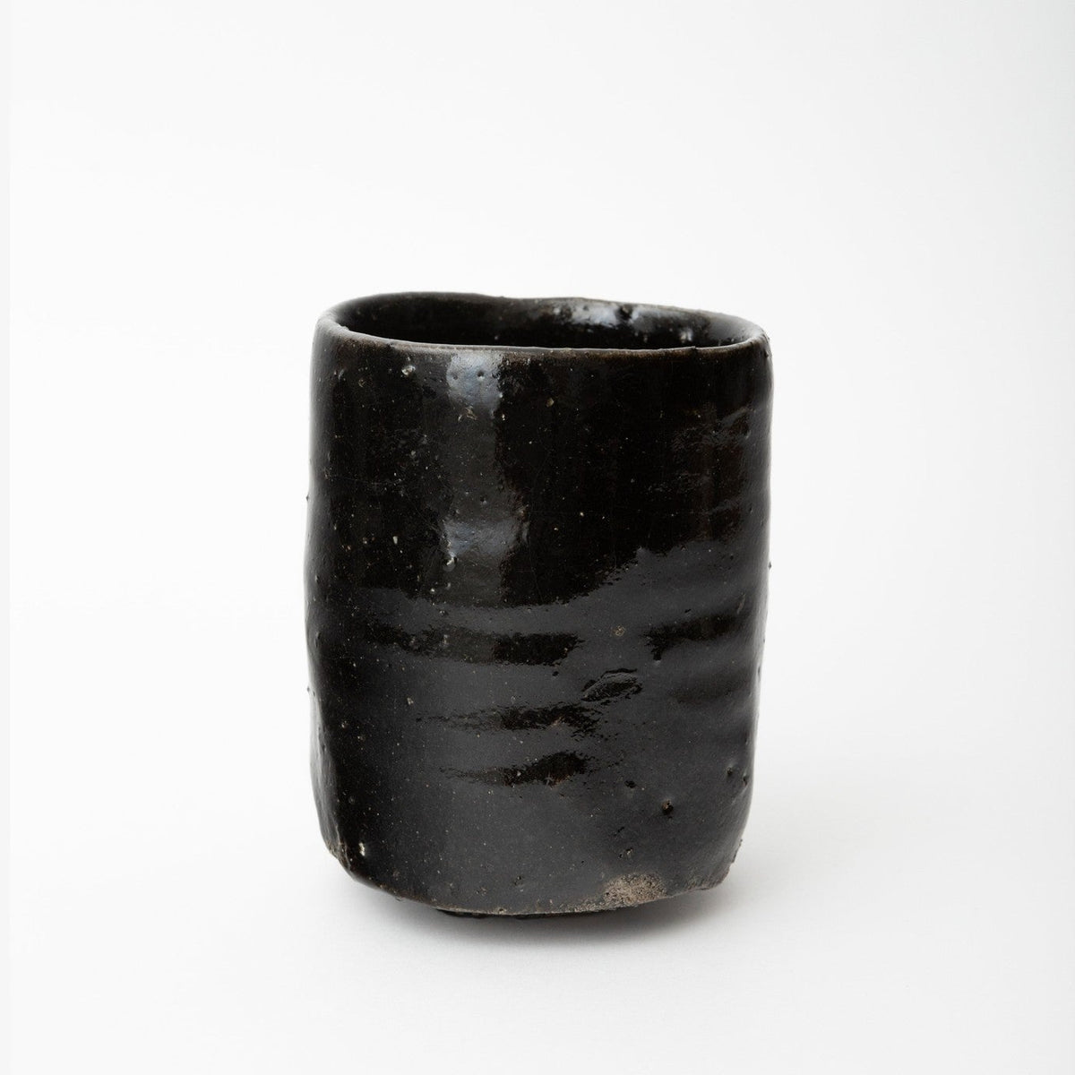 Three-quarter view of the cup showing the slight ripple in the walls and the pale band of bare clay at the base.
