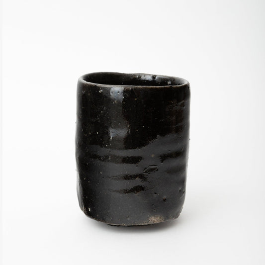 Three-quarter view of the cup showing the slight ripple in the walls and the pale band of bare clay at the base.