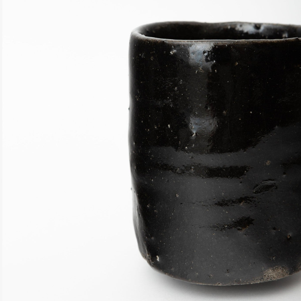 Detail of the cup's shoulder and rim from the side, the wet black glaze in strong light.