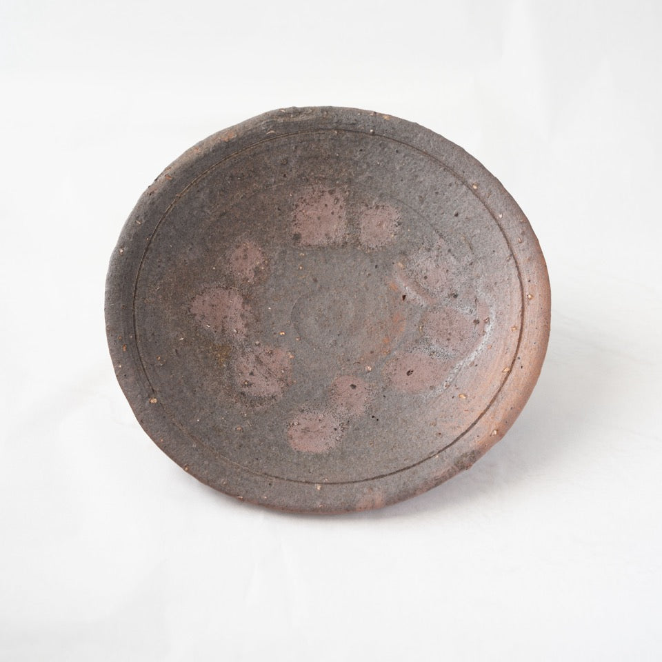 Front view of a dark charcoal-grey yakishime plate by Kai Tsujimura, showing a subtle circular fire mark and an incised inner rim line.